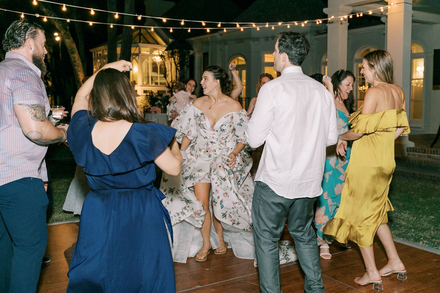 People dancing and celebrating at a nighttime outdoor party with string lighting.