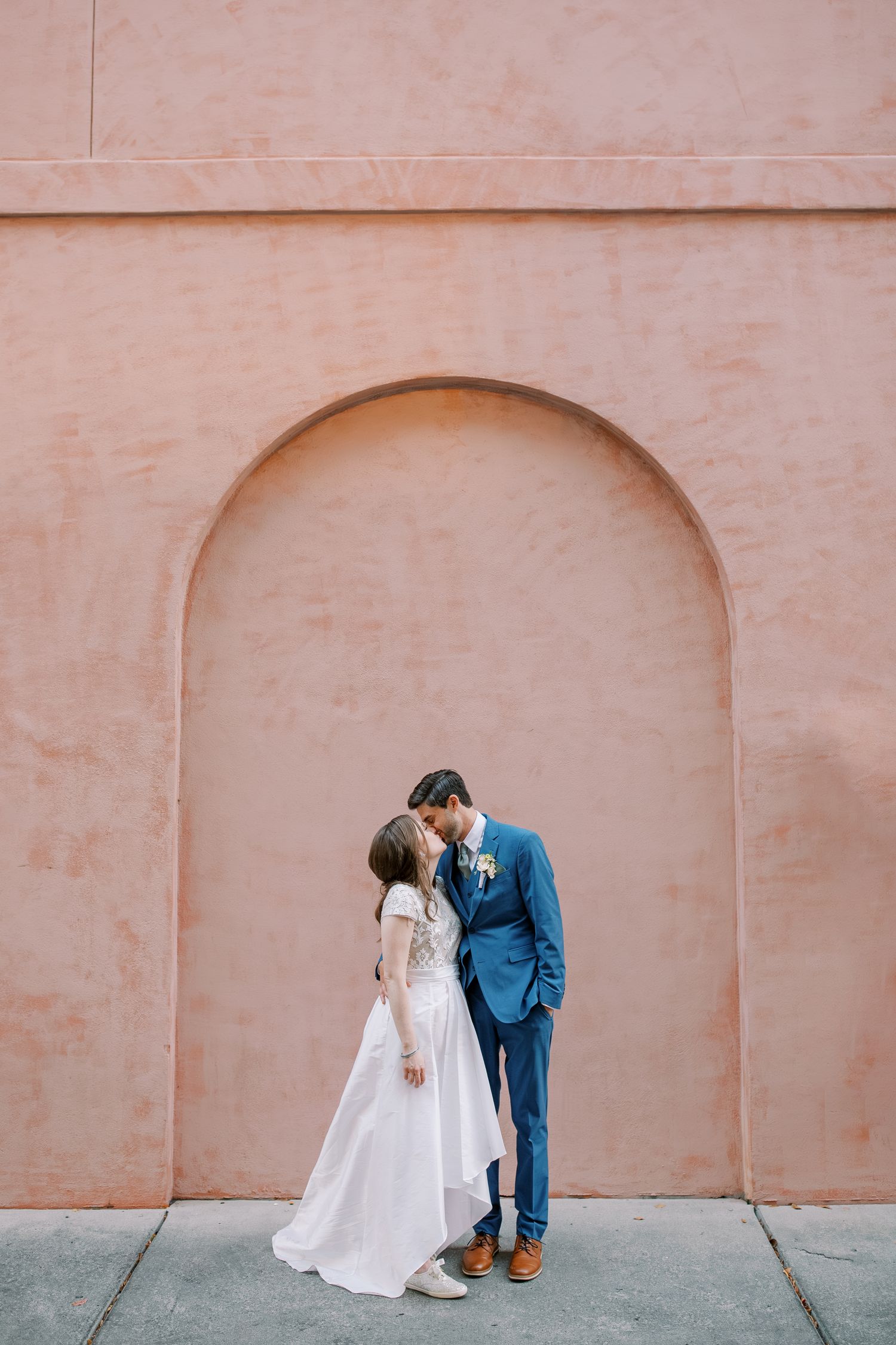 Wedding couple poses for romantic photos against a peach colored wall with arched alcoves.