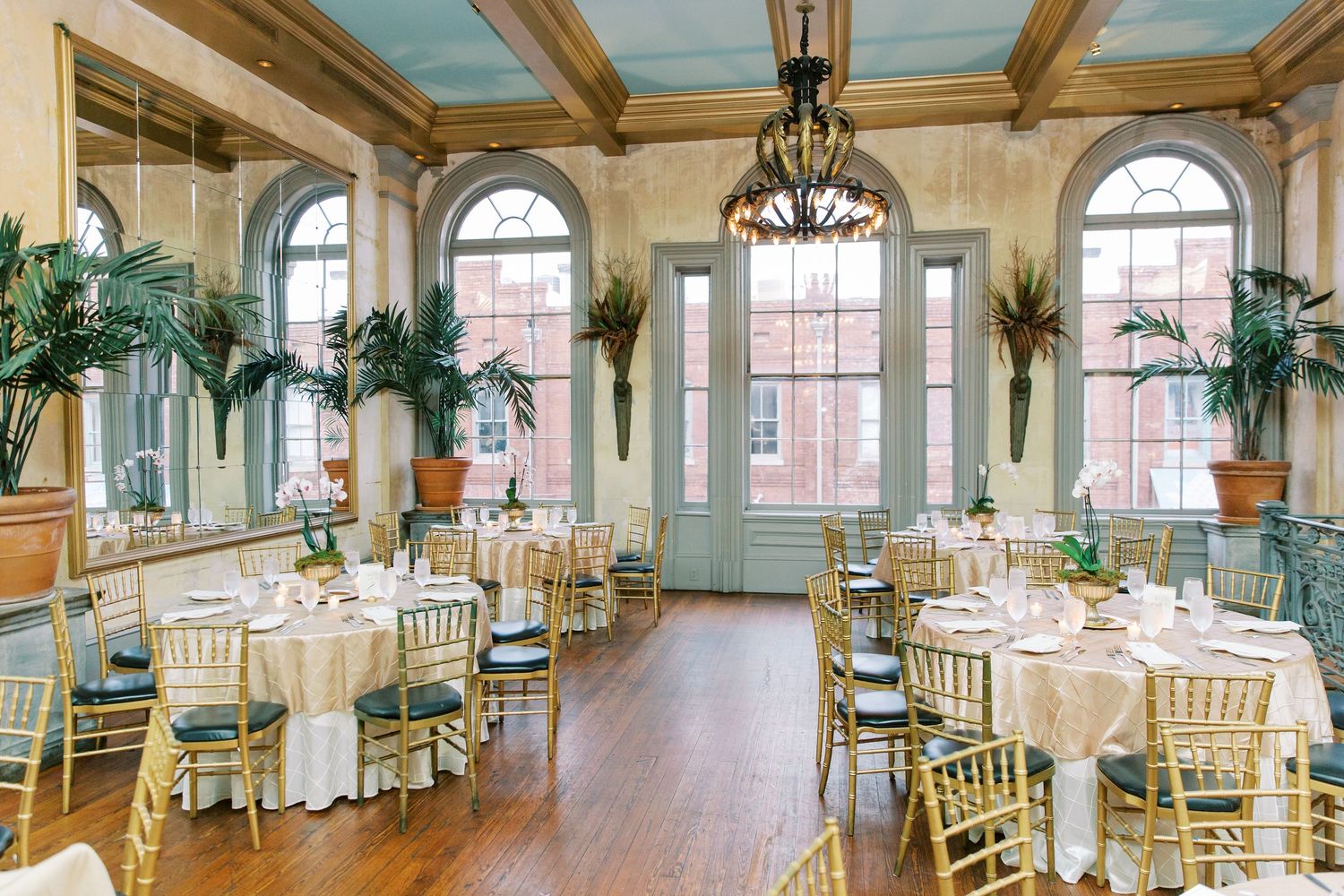 Elegant ballroom with arched windows, hardwood floors, golden chiavari chairs and round tables set for an upscale event at Garibali