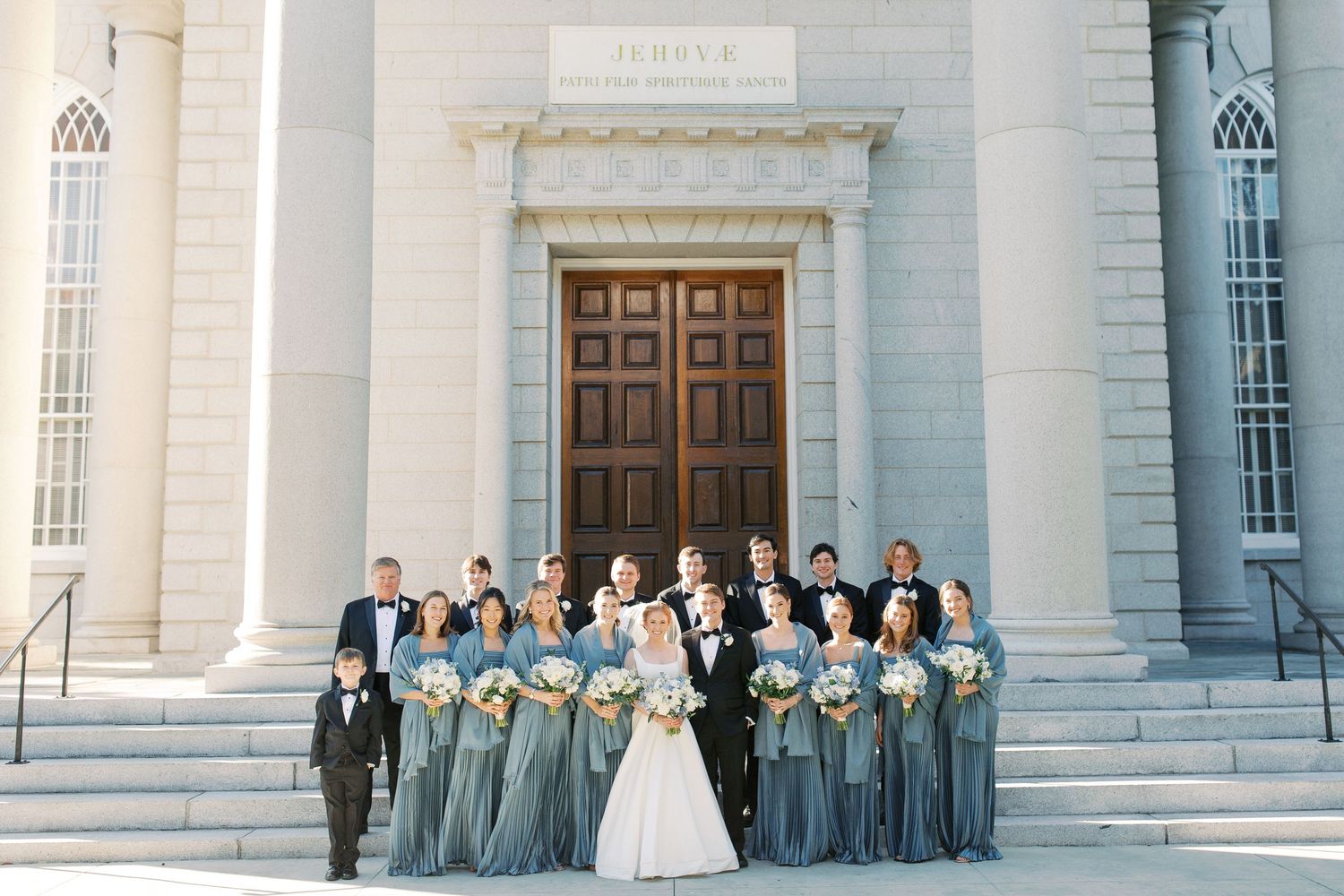 Wedding party posed on grand white stone steps with bridesmaids in blue dresses.