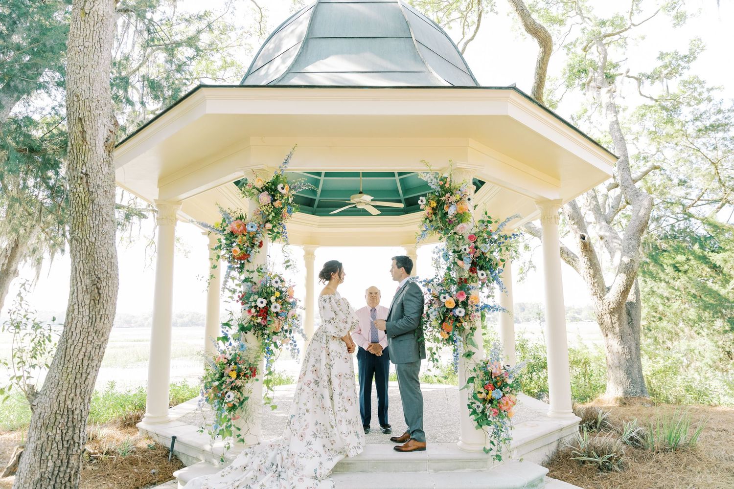 Intimate outdoor wedding ceremony in an octagonal gazebo adorned with fresh flowers and greenery.