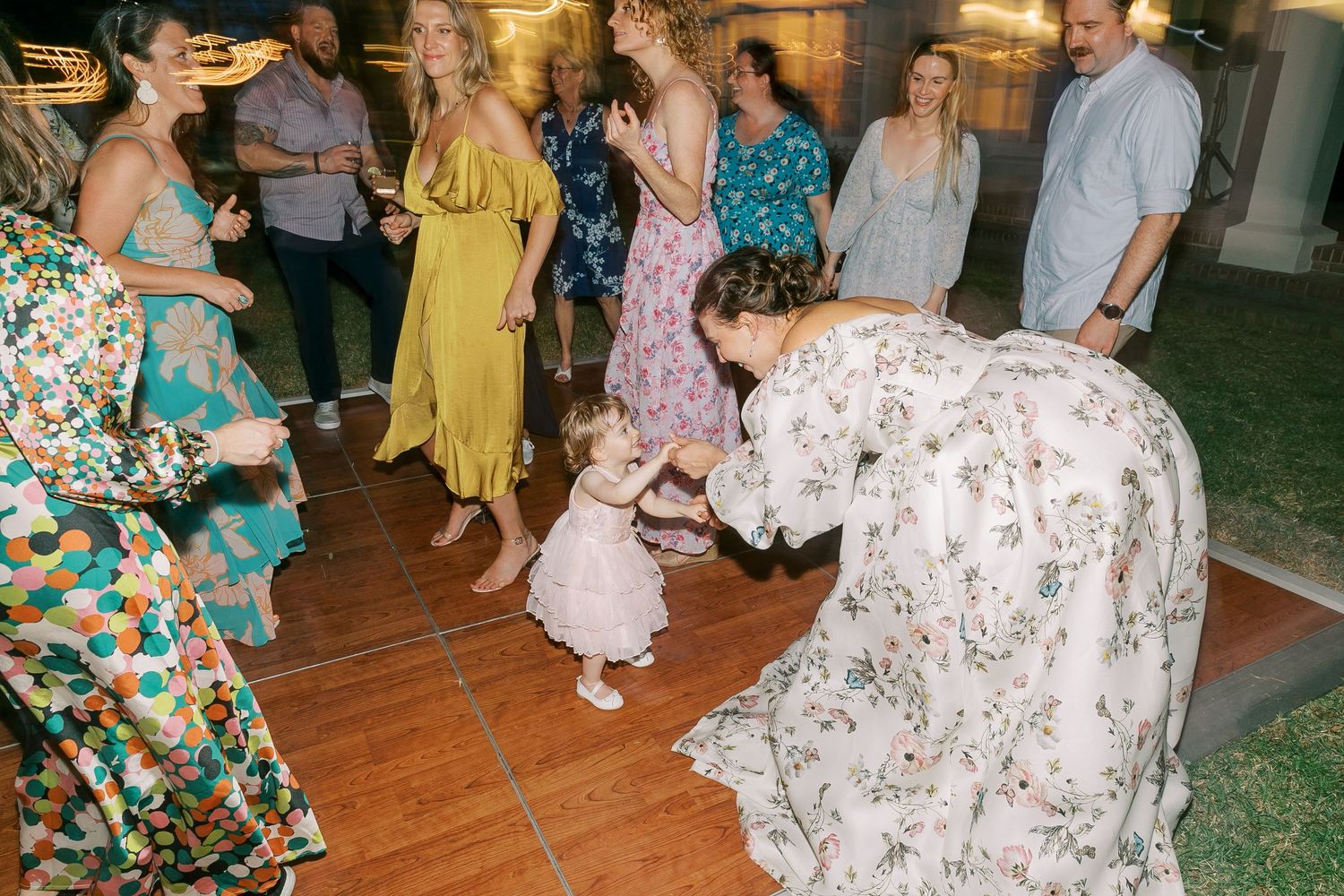 Wedding reception guests dancing on a wooden floor during evening celebrations.