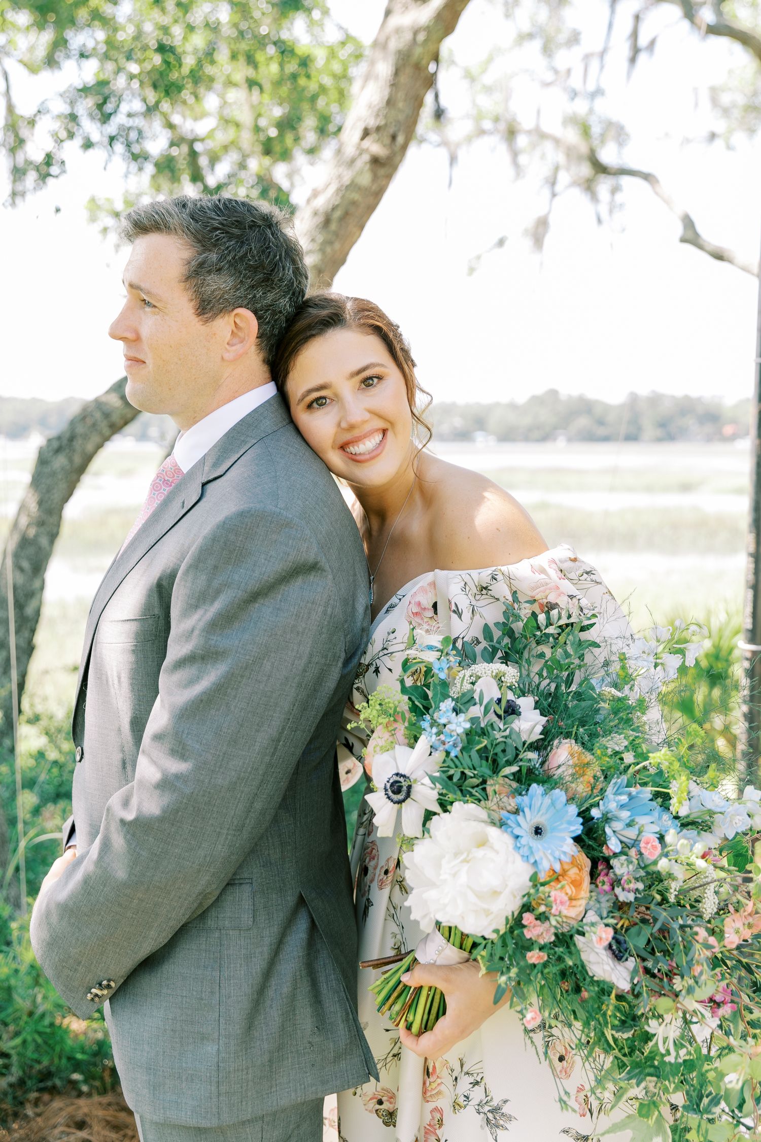 A couple shares a sweet moment outdoors surrounded by beautiful floral bouquets and greenery at their wedding.