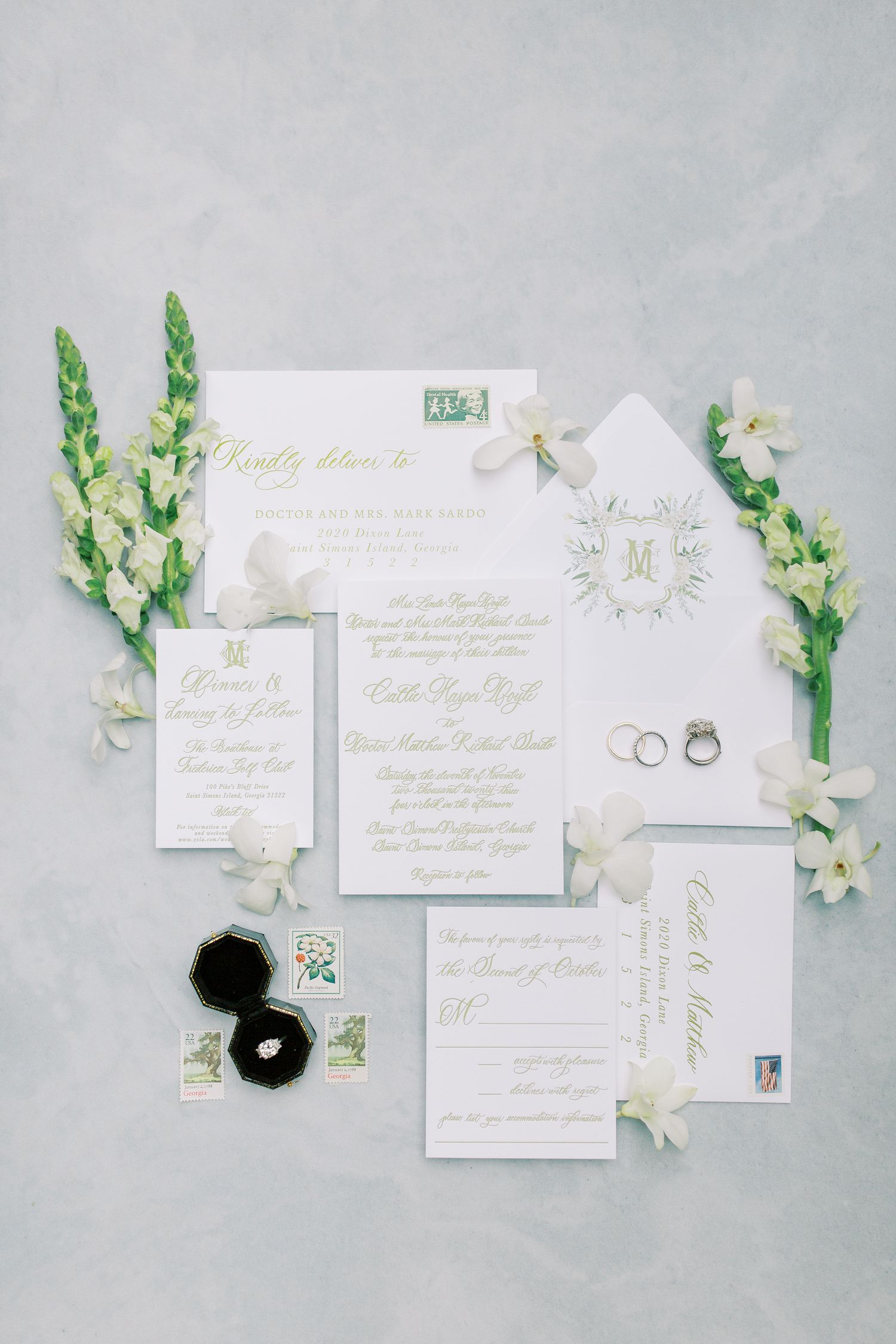 Wedding invitation suite in white and gold with floral accents and wedding rings.