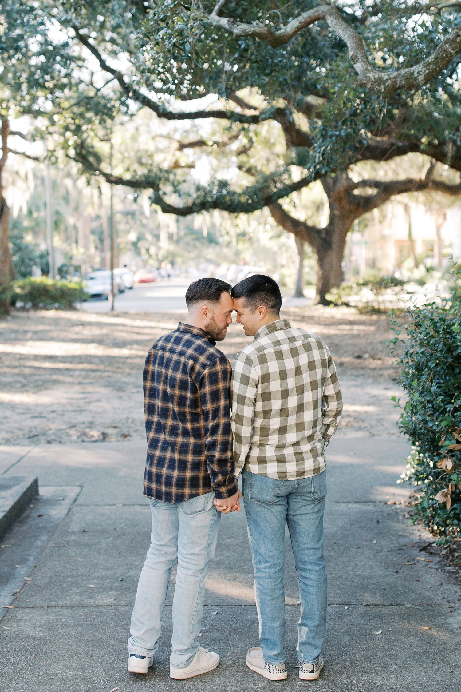 Romantic gay couple moment under Spanish moss trees wearing coordinating plaid shirts in Forsyth Park.
