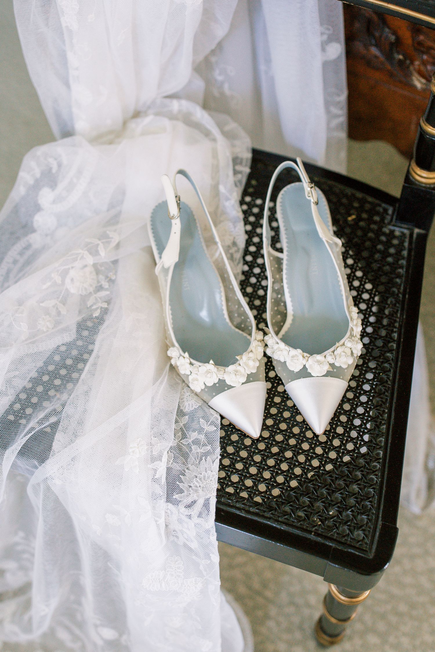 Elegant white bridal shoes with pearl embellishments displayed alongside delicate tulle veil on a black surface.