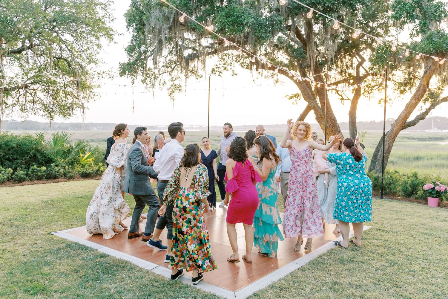Wedding guests gather for outdoor celebrations under trees at a scenic venue.