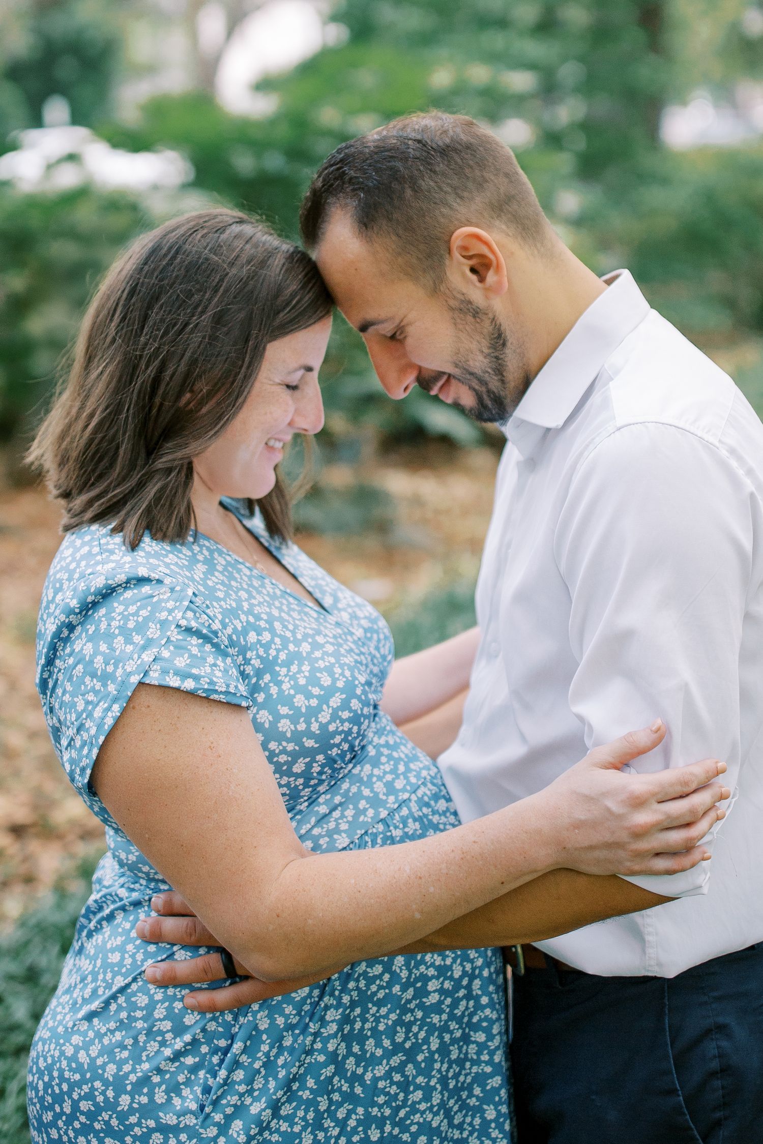 A tender maternity photoshoot showing a couple embracing in a natural outdoor setting.