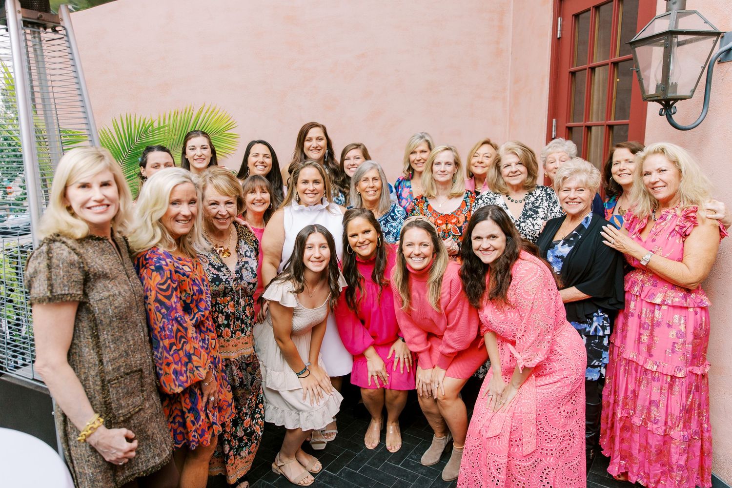 A cheerful group of people in colorful dresses and outfits gather together for a celebratory photo outside The Pink House.