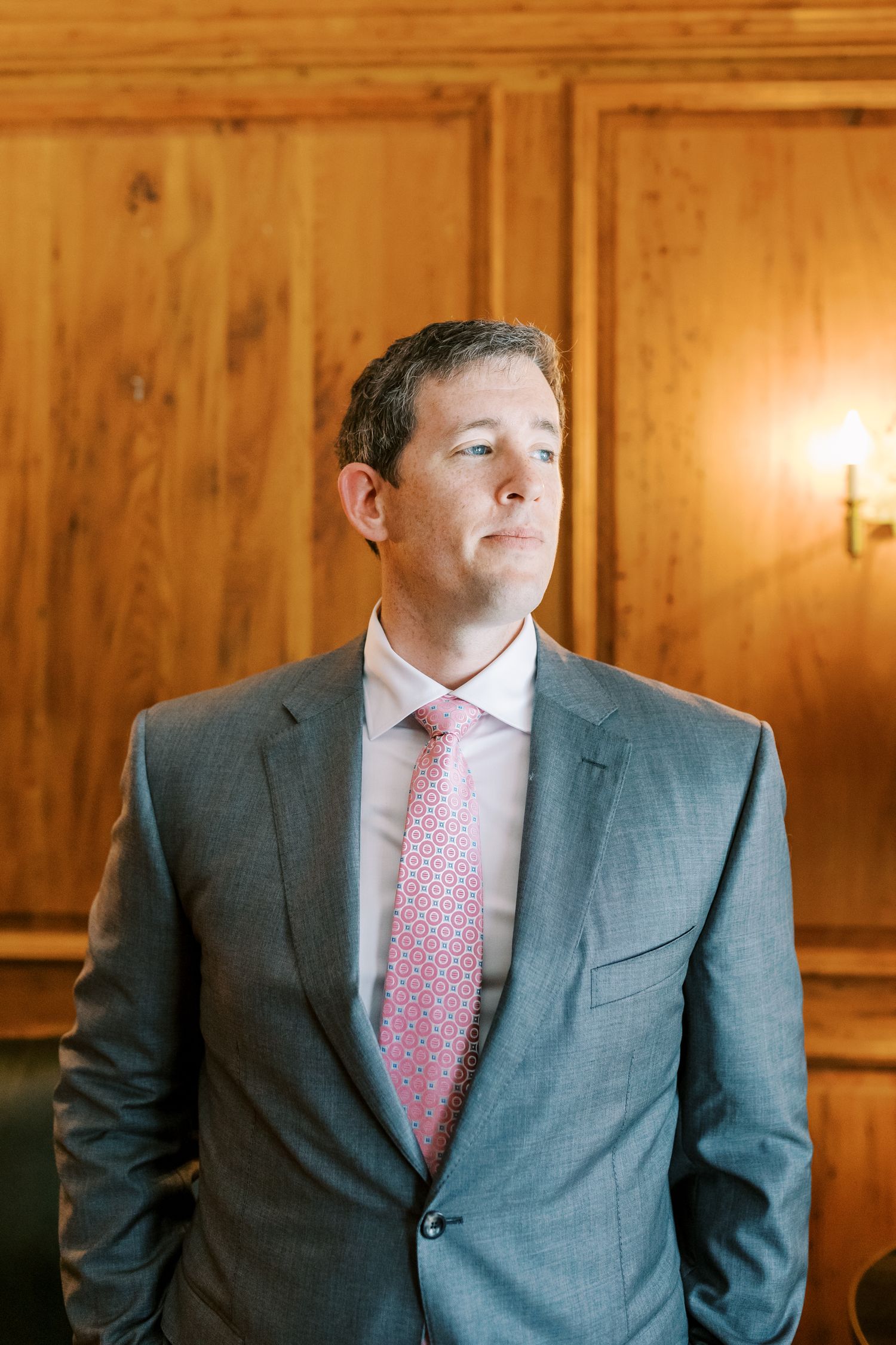 A sequence of images showing a groom in a grey suit and pink tie looking contemplative against wooden paneling.