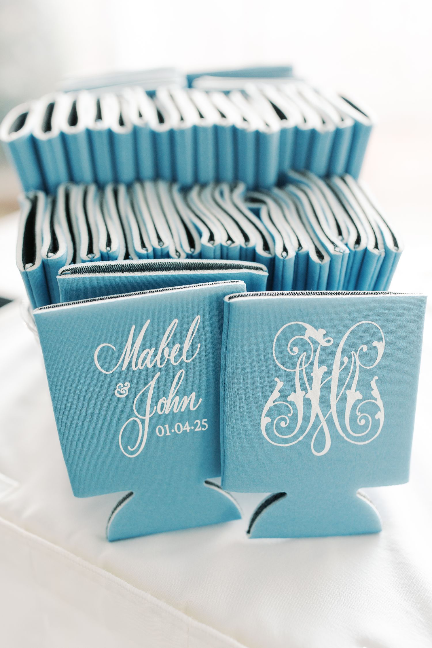 Light blue wedding drink koozies with custom white monogram designs lined up in rows.