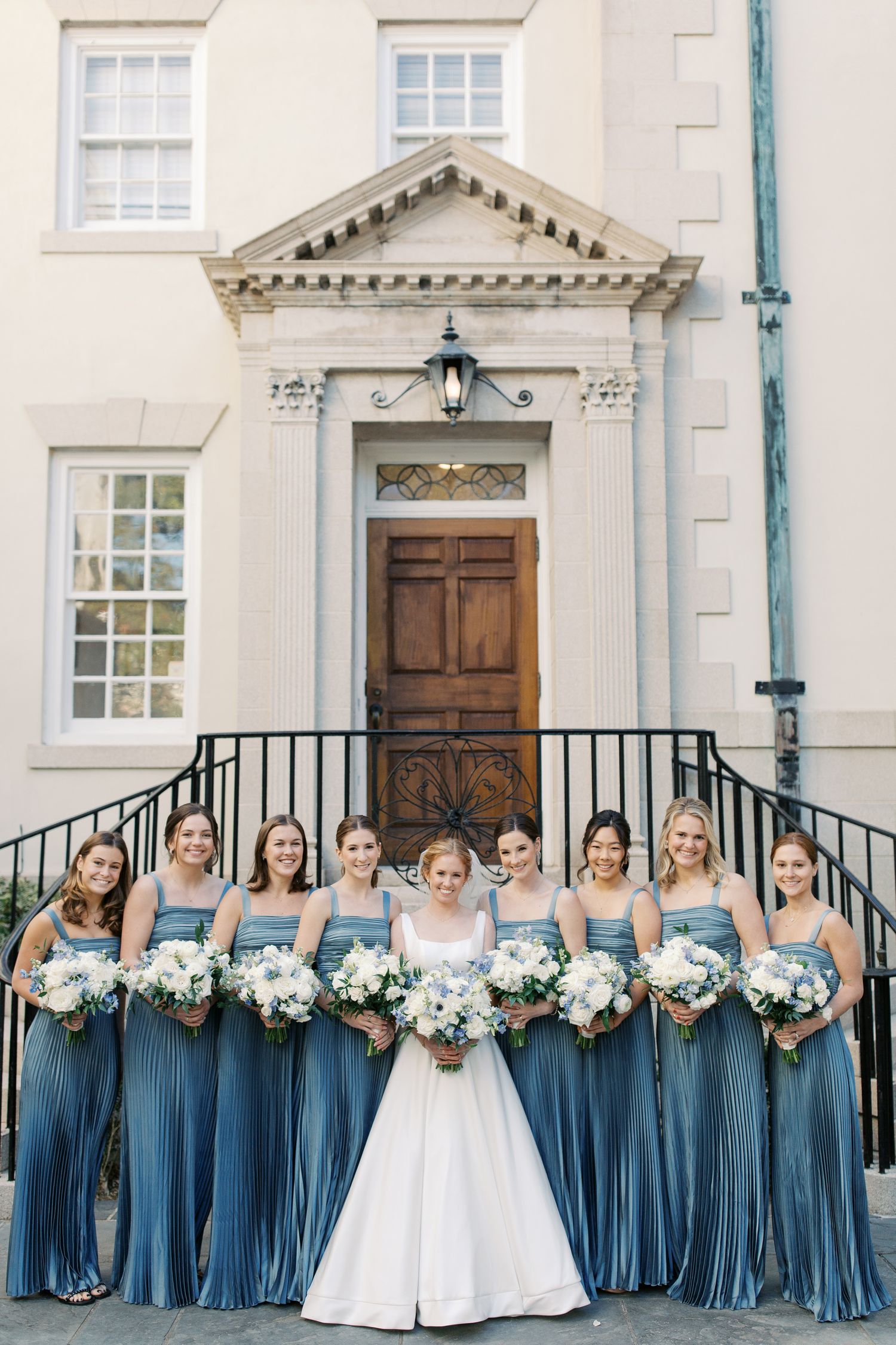 Bridesmaids in blue dresses lined up with bouquets on building steps.