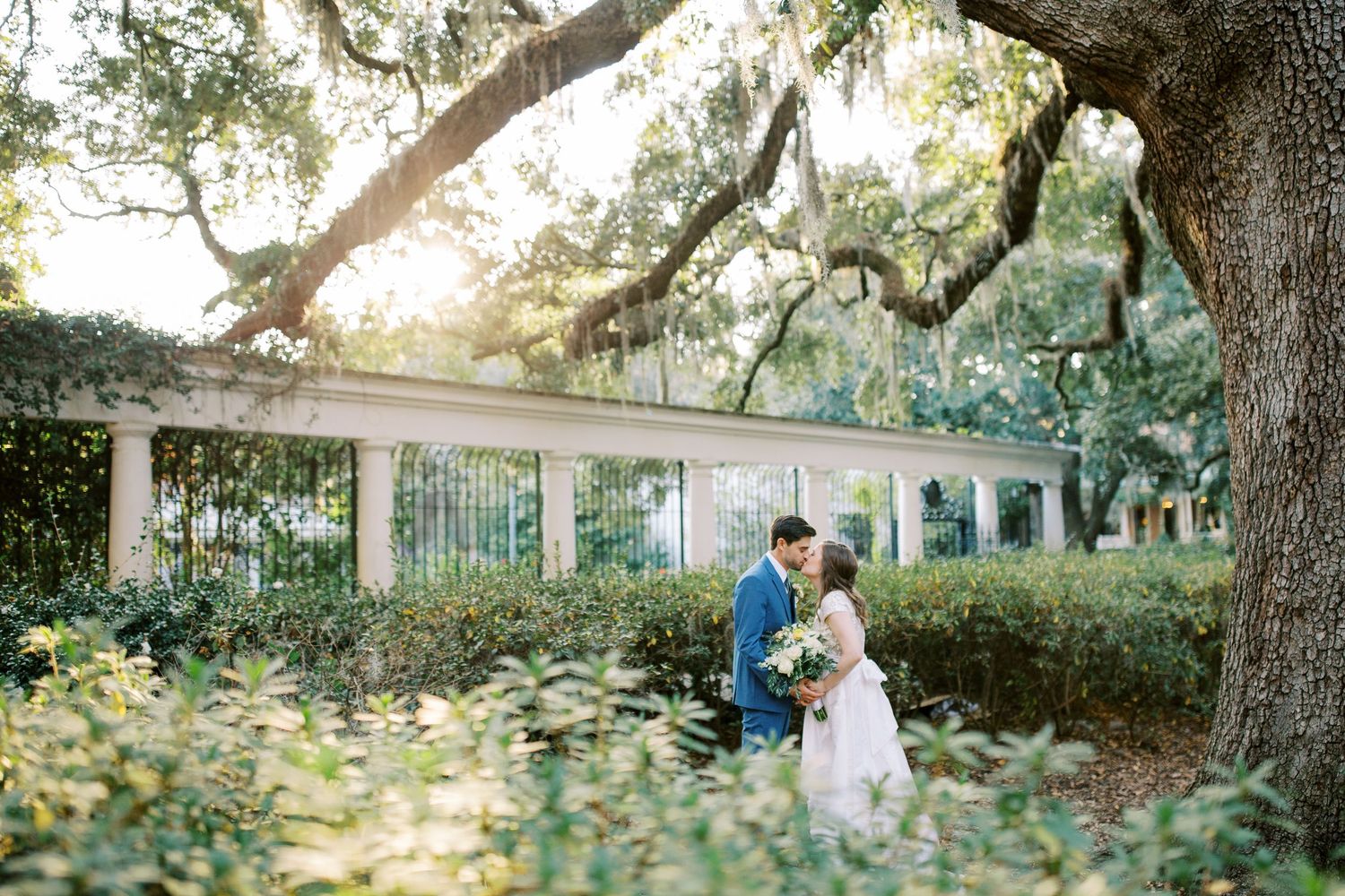 Romantic wedding portrait under Spanish moss-draped oak trees in garden setting.