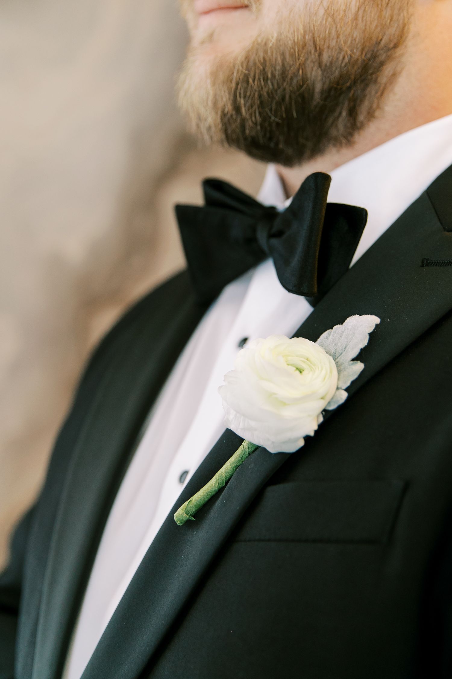 A classic black tuxedo with white shirt and bowtie adorned with an elegant white ranunculus boutonniere.