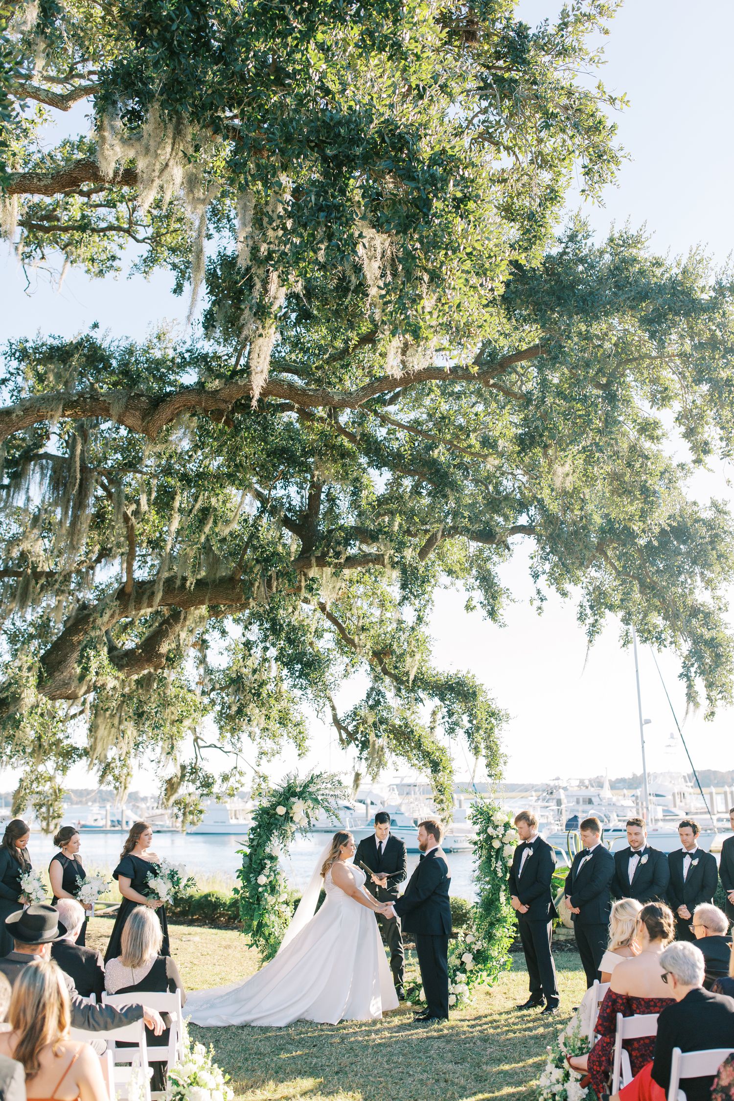 Outdoor wedding ceremony under a majestic Spanish moss-draped oak tree beside a waterfront in Savannah.