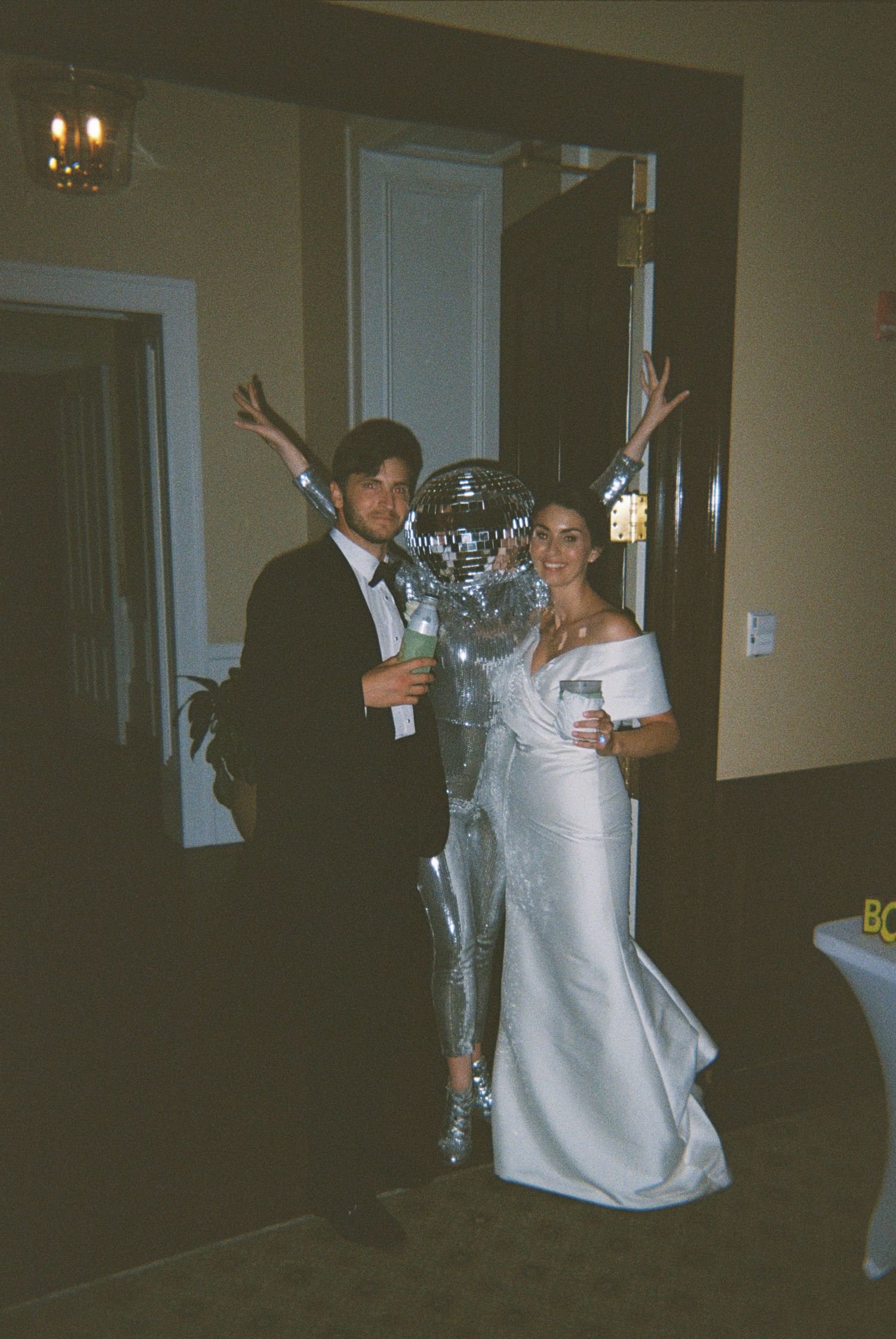 Couple in white attire dancing joyfully at a wedding reception in a dimly lit venue.