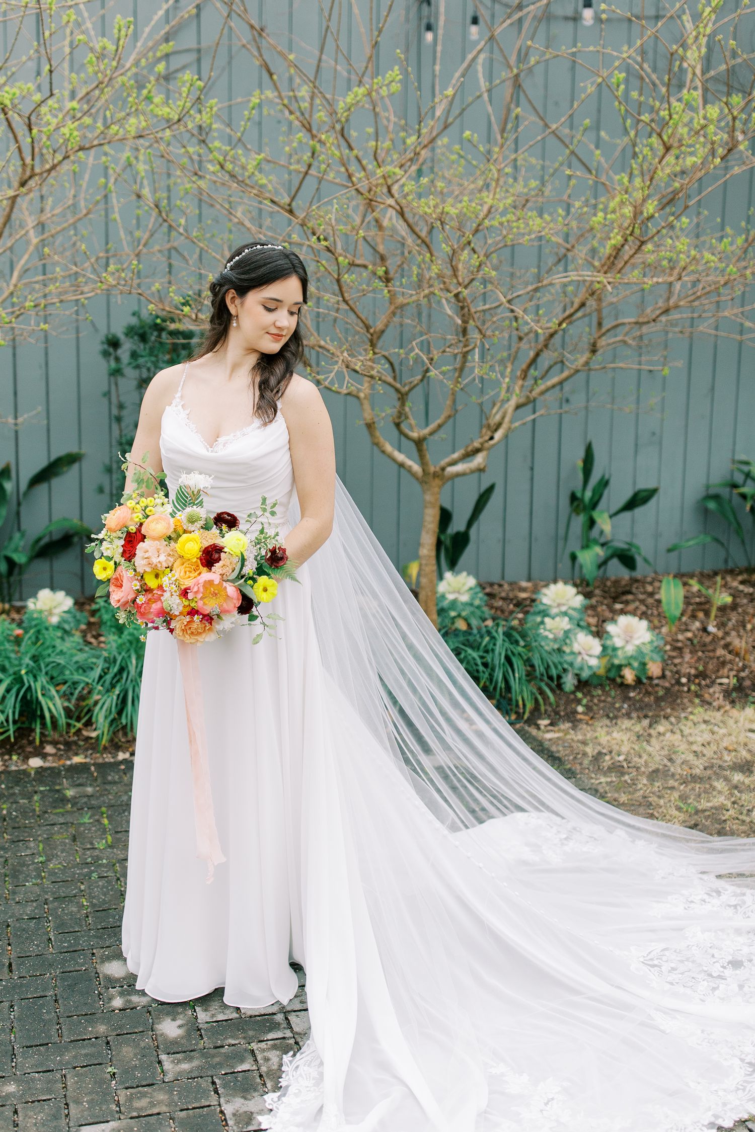 A bride in a flowing white gown holds a vibrant bouquet of flowers in a garden setting.