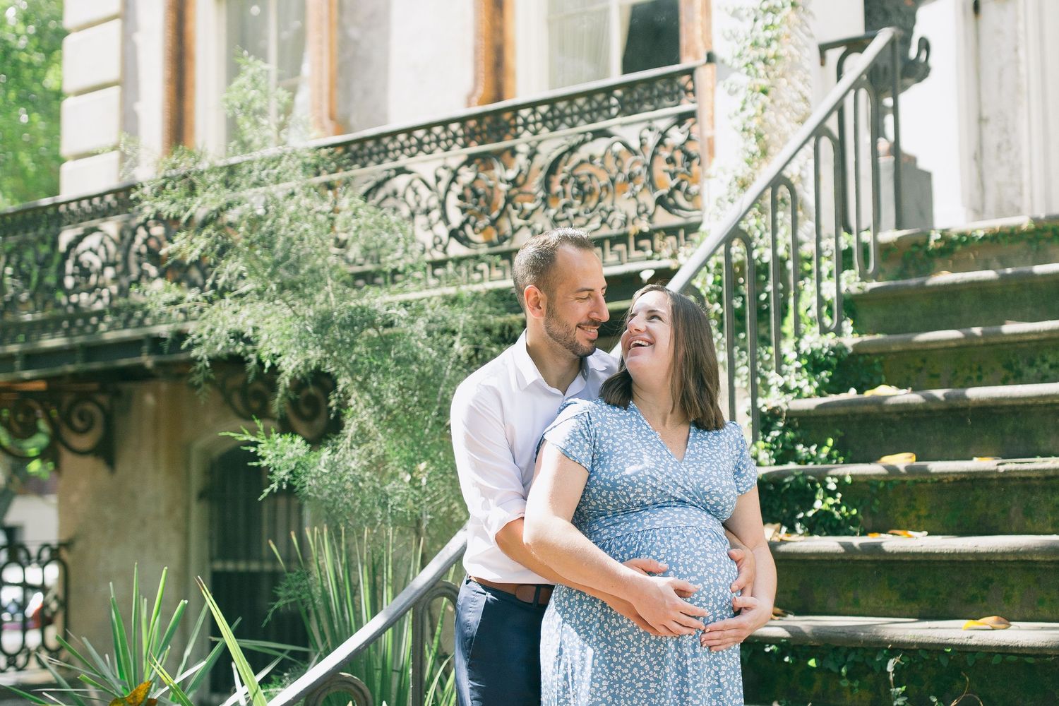 Expectant couple embraces during maternity photoshoot in a lush garden setting with stone steps and greenery.