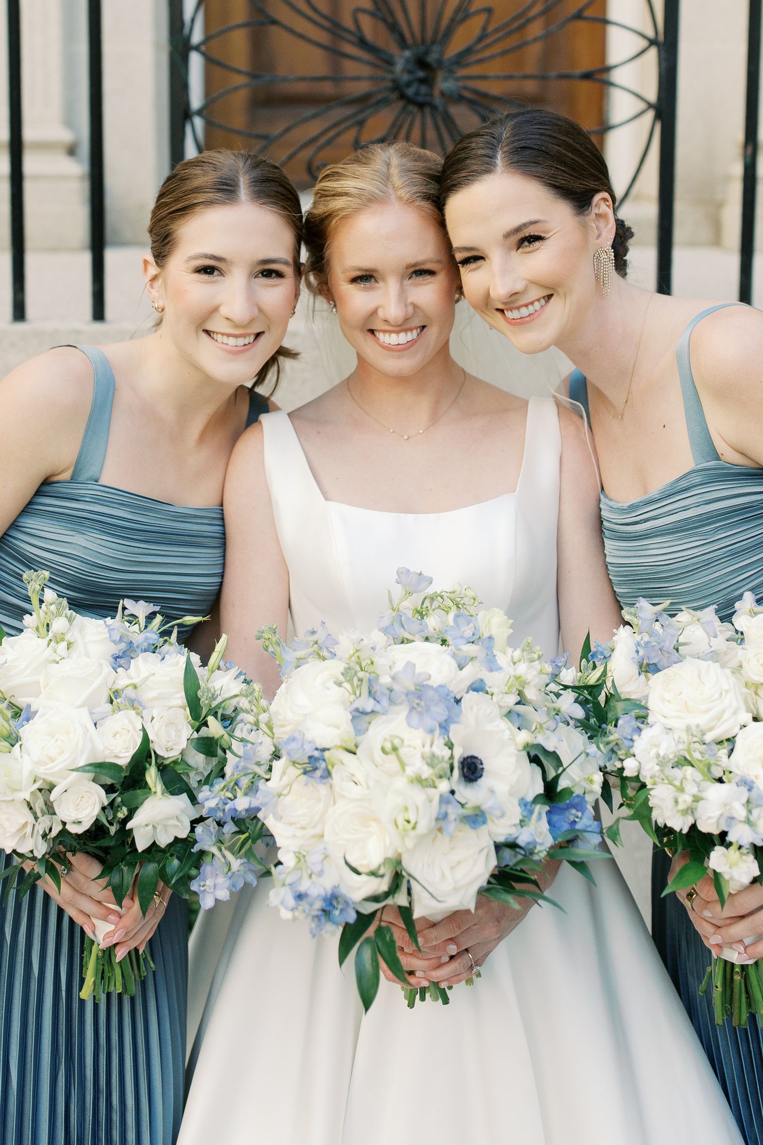 Bridesmaids in dusty blue dresses holding white and blue floral bouquets.