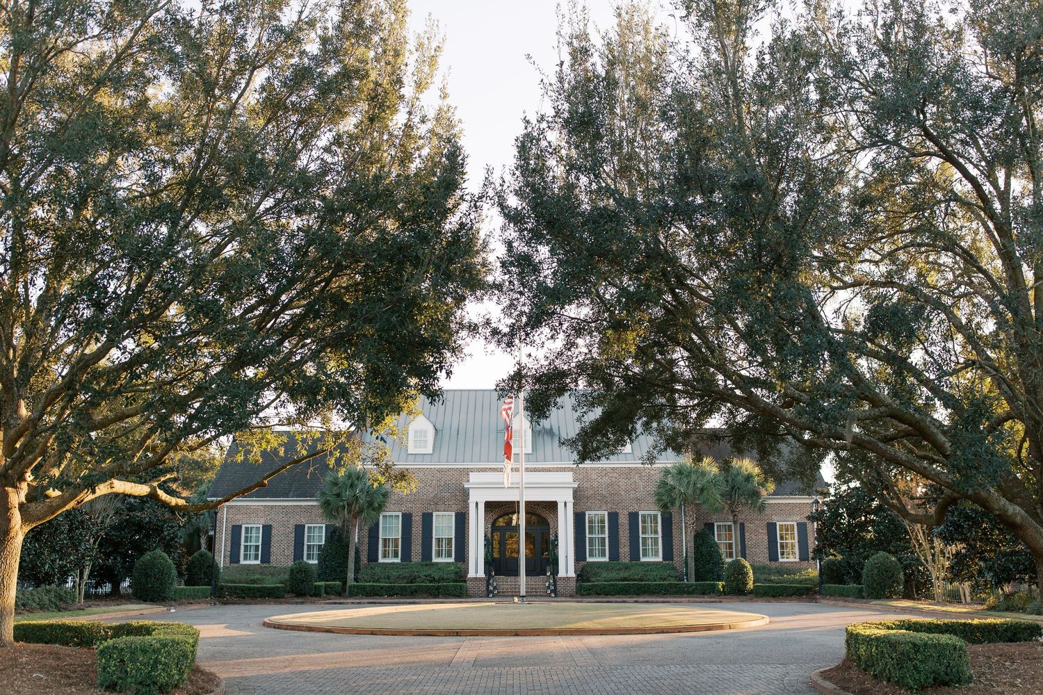 Elegant white colonial style mansion with grand columns framed by mature oak trees.