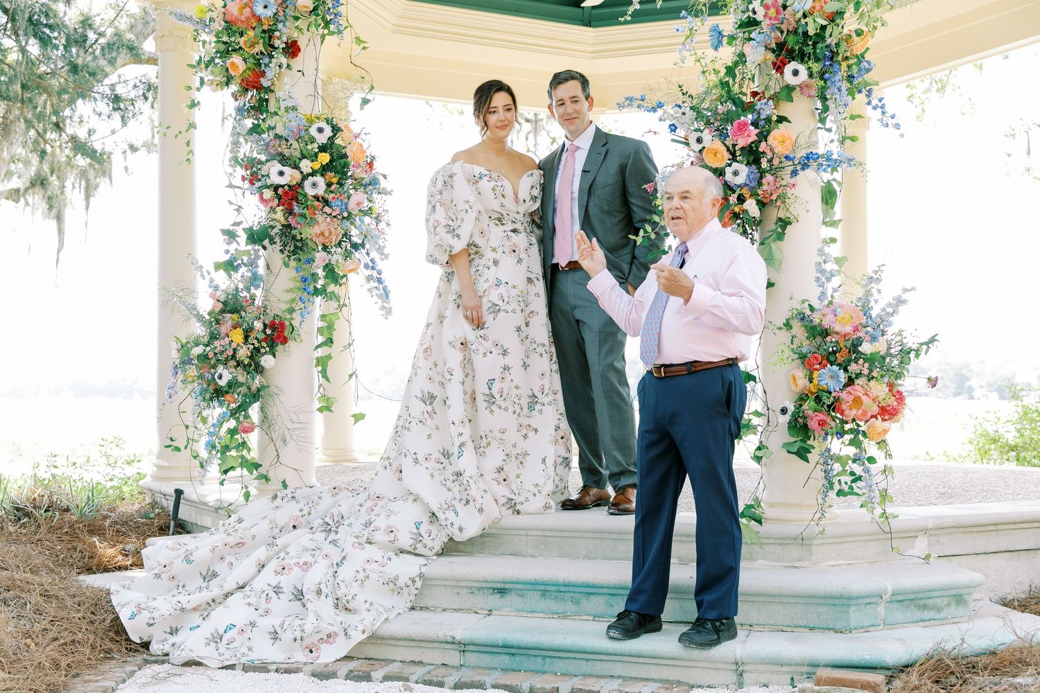 Wedding ceremony under a decorated gazebo with floral arrangements and a beautiful train dress.