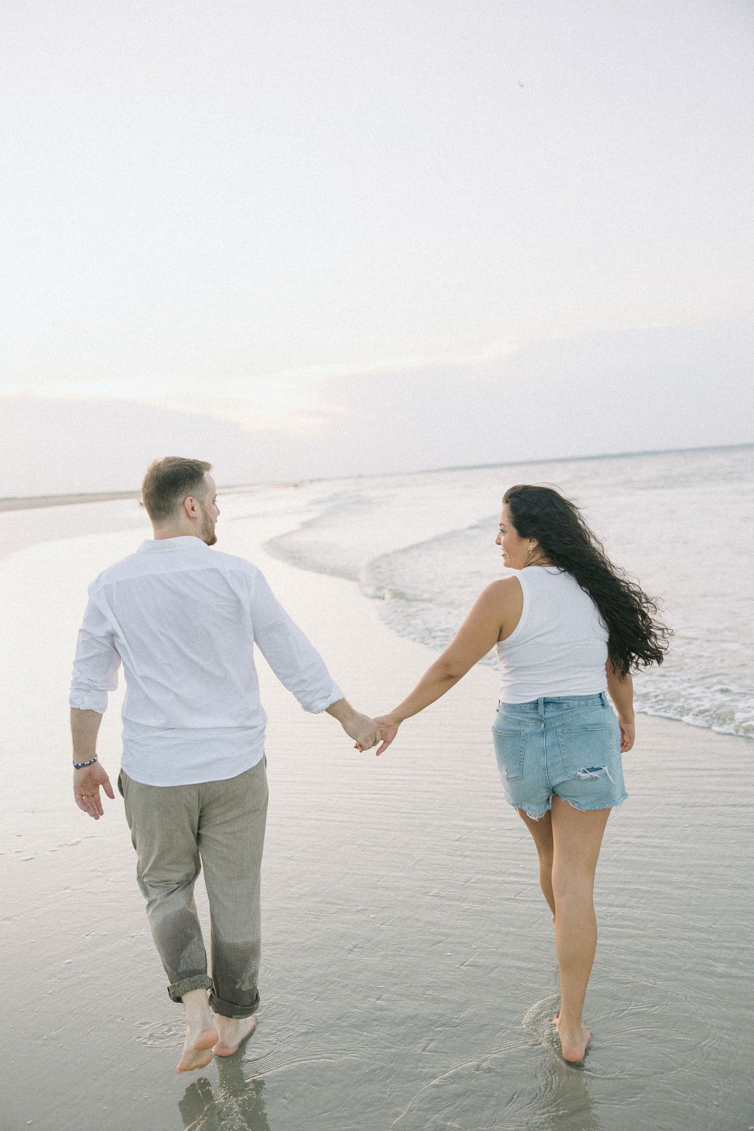 Two people wading in shallow ocean water while holding hands at dusk.
