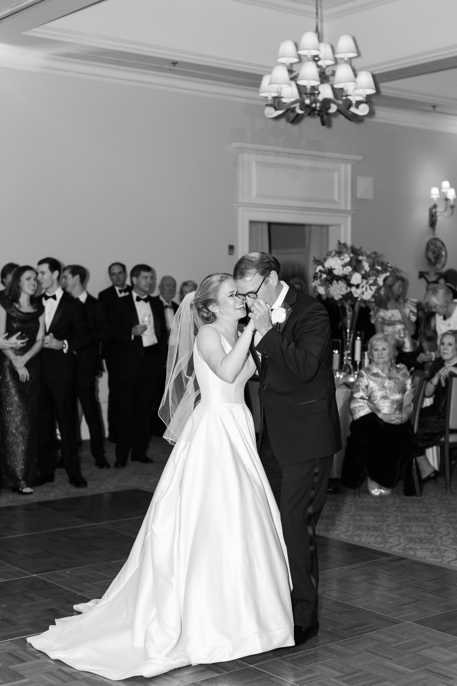 Black and white photo of couple sharing their first dance in an elegant ballroom setting.