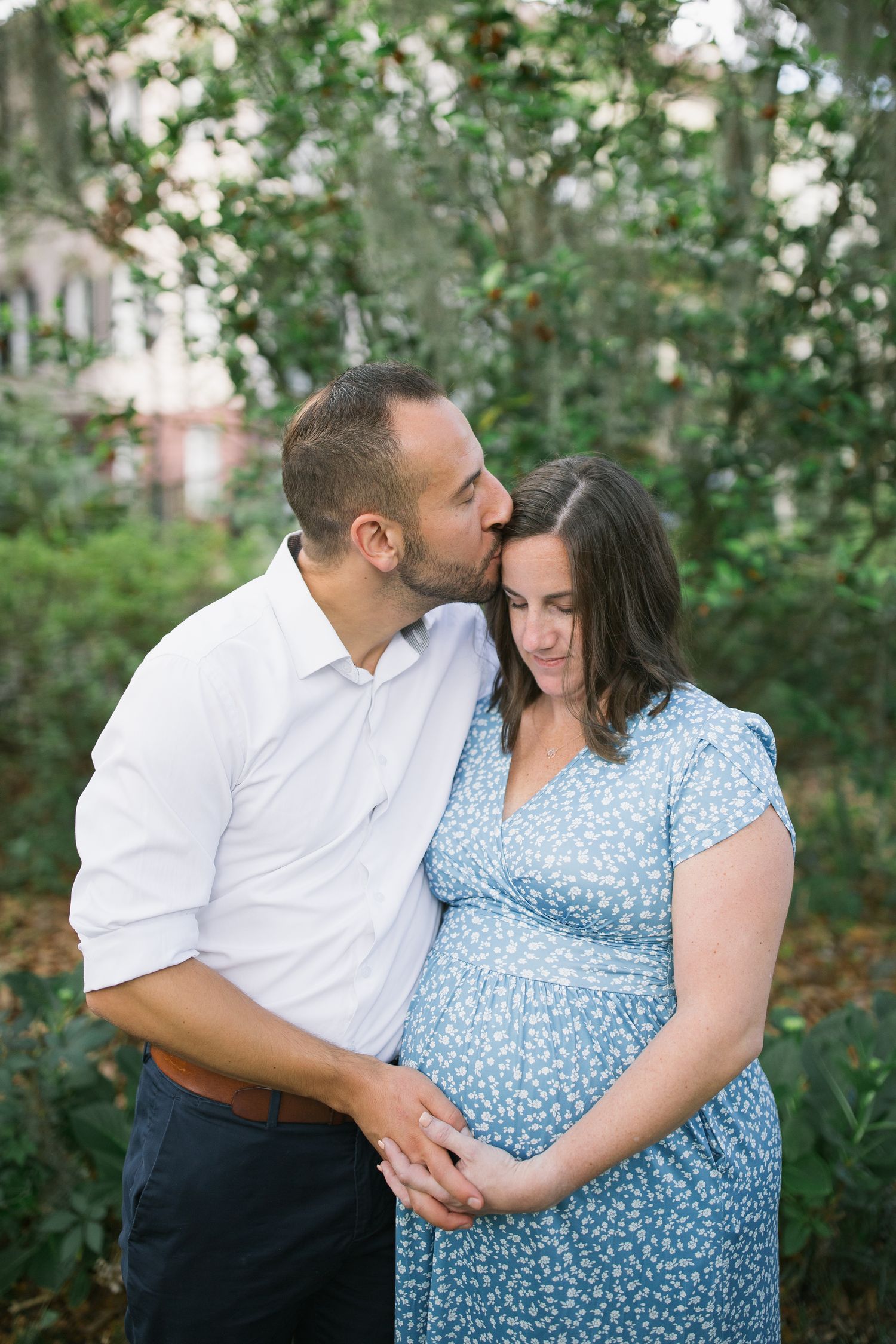 A couple shares tender moments in a garden setting wearing white and blue polka dot outfits.