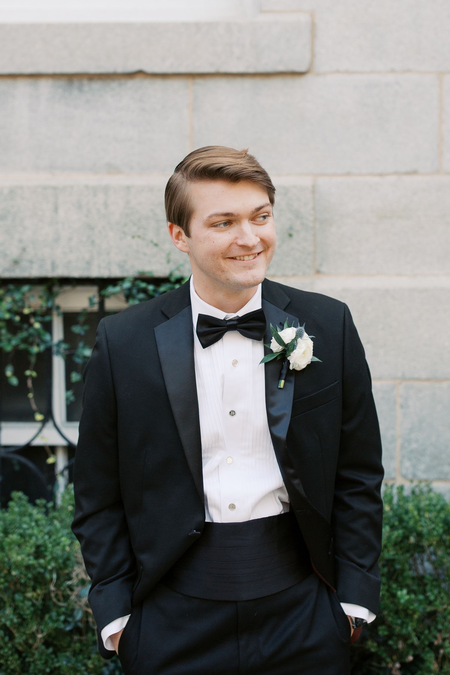 A formal portrait of a groom in classic black tuxedo with bow tie and boutonniere.
