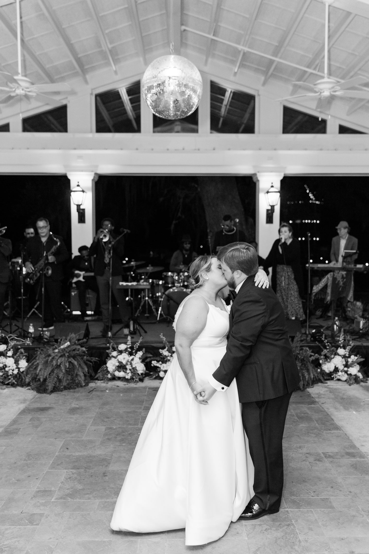 Black and white photo of a wedding couple's first dance under a disco ball with band performing in background.