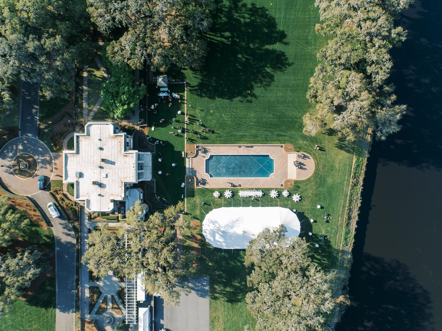 Aerial view of a white house with swimming pool and dome structure in a landscaped backyard surrounded by trees.