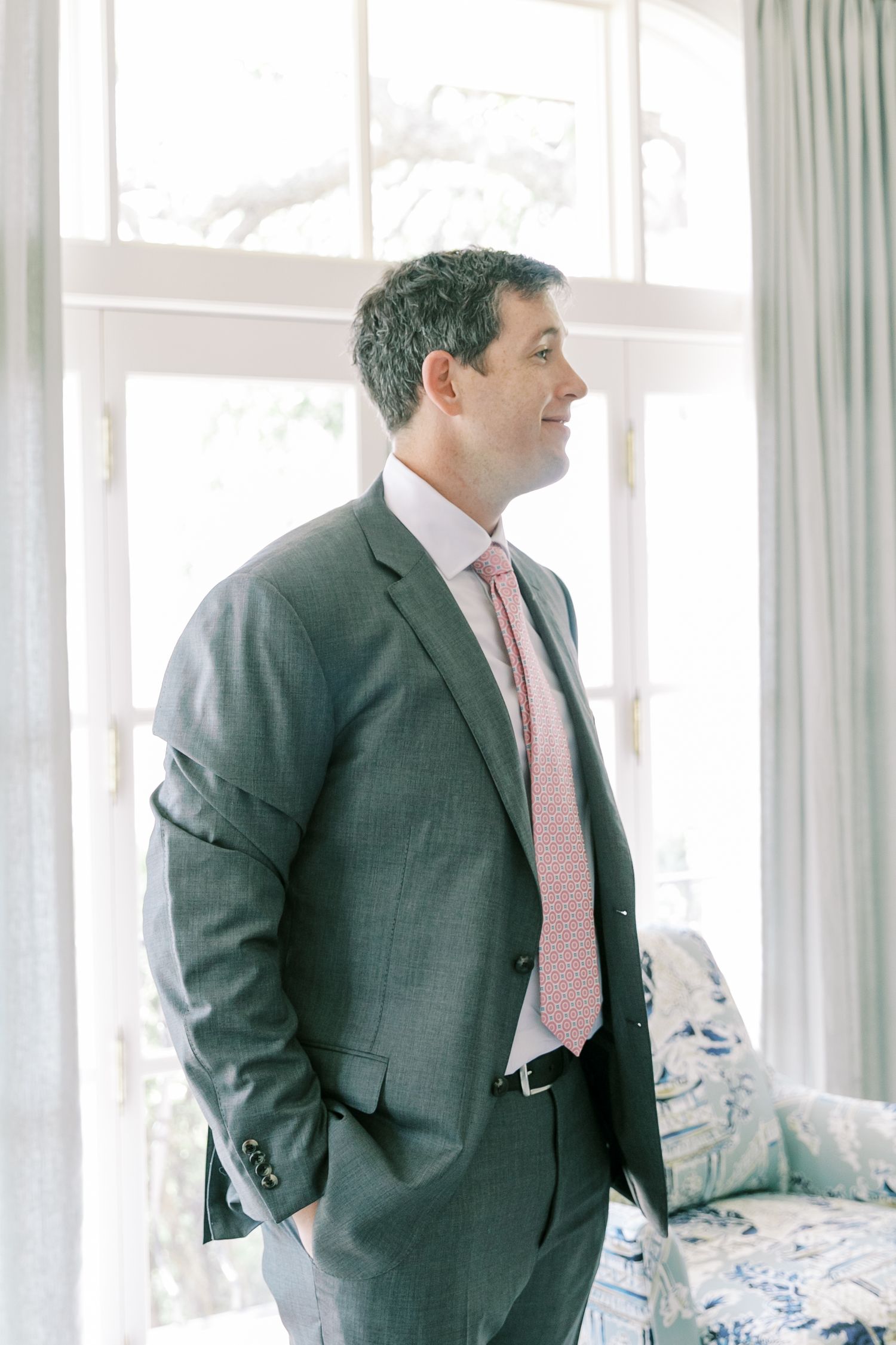 Multiple images of a man in a gray suit and pink tie looking out windows in an elegant room.