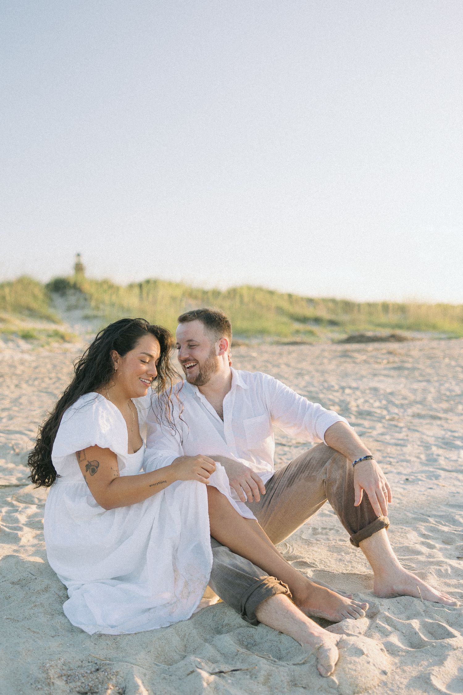 Couple sharing romantic moments while sitting on sandy beach during golden hour.