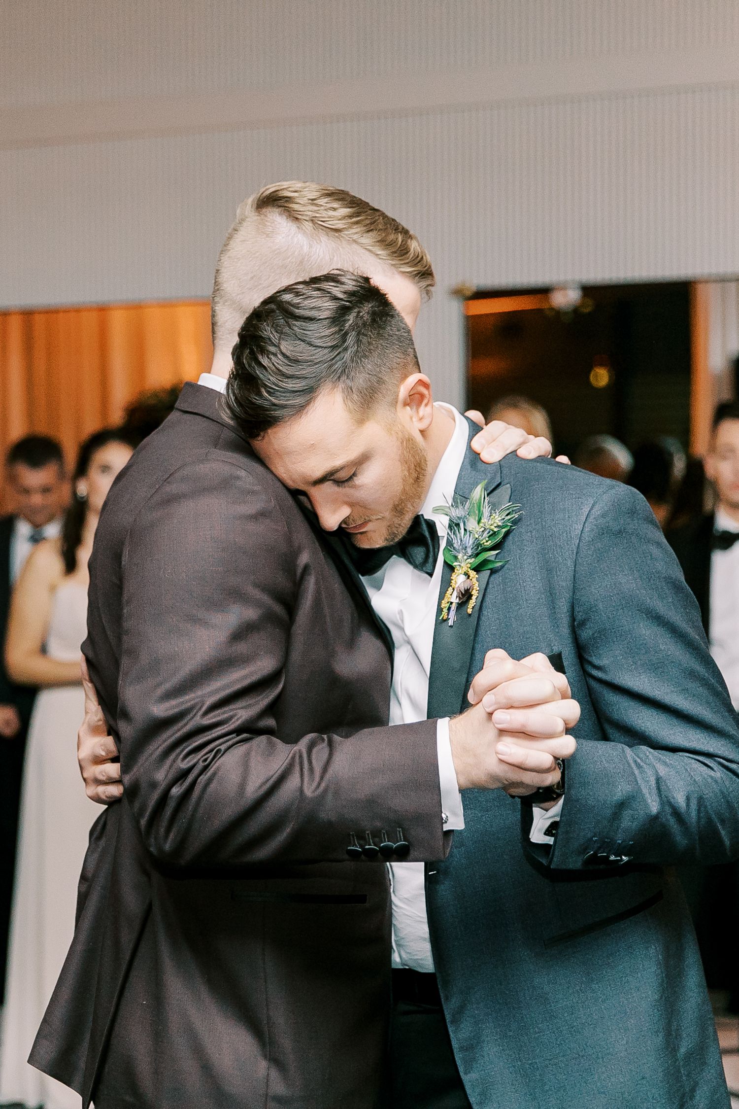 A tender moment at a wedding as two grooms in formal suits embrace during their dance together.