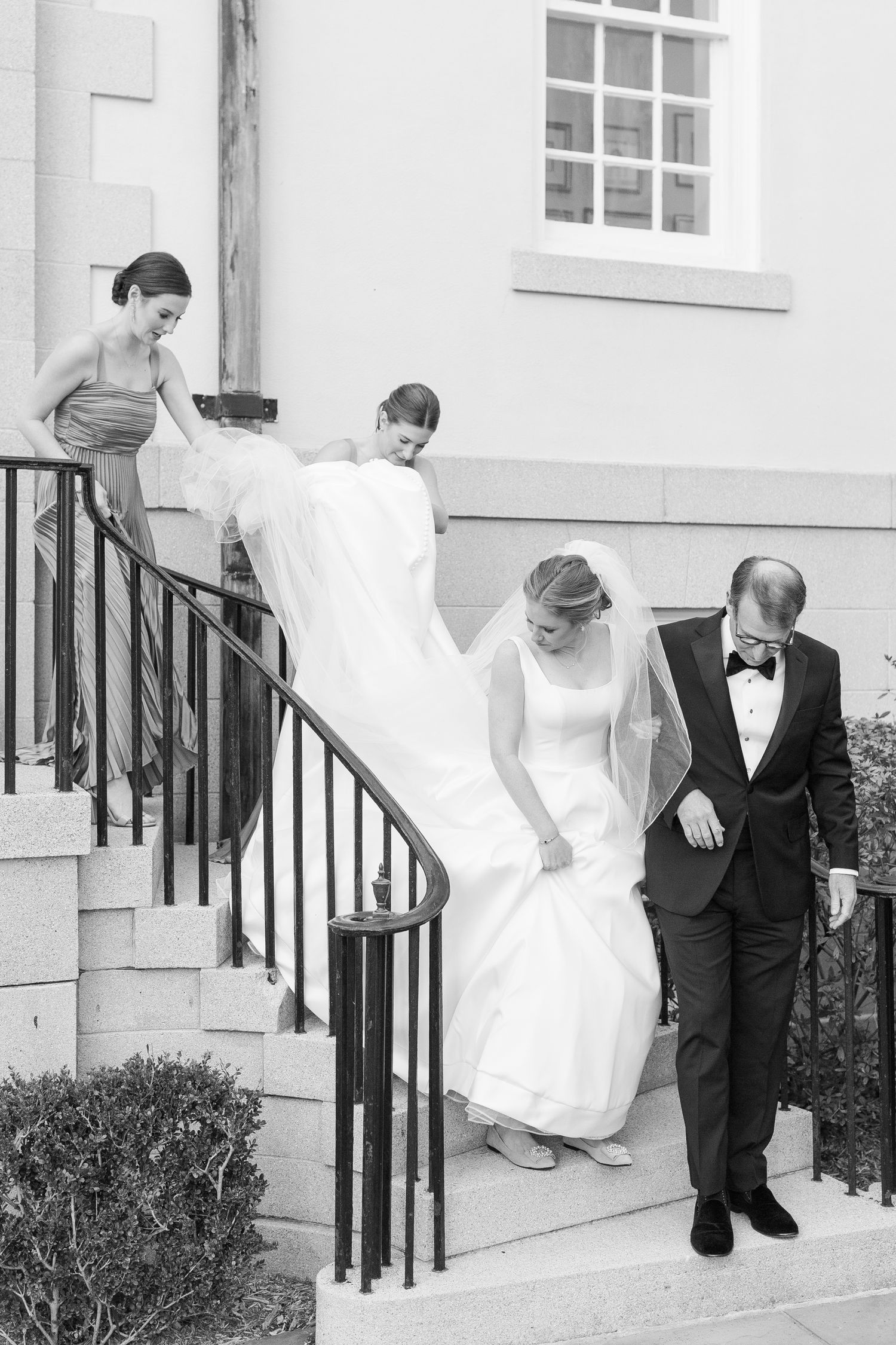Wedding party descending white building steps with flowing bridal gown.