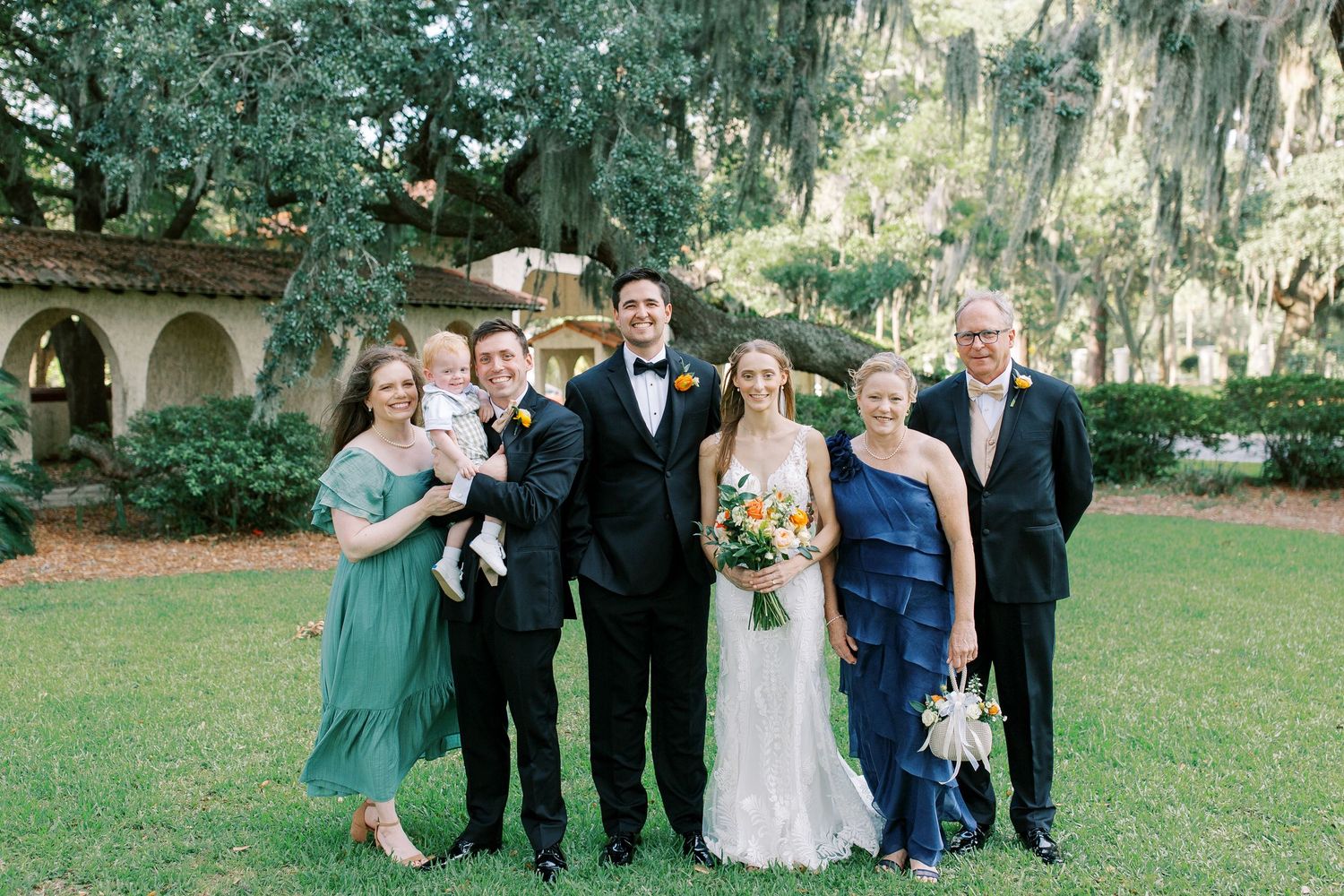 Wedding party poses together on a lush green lawn with Spanish moss draped trees in the background.