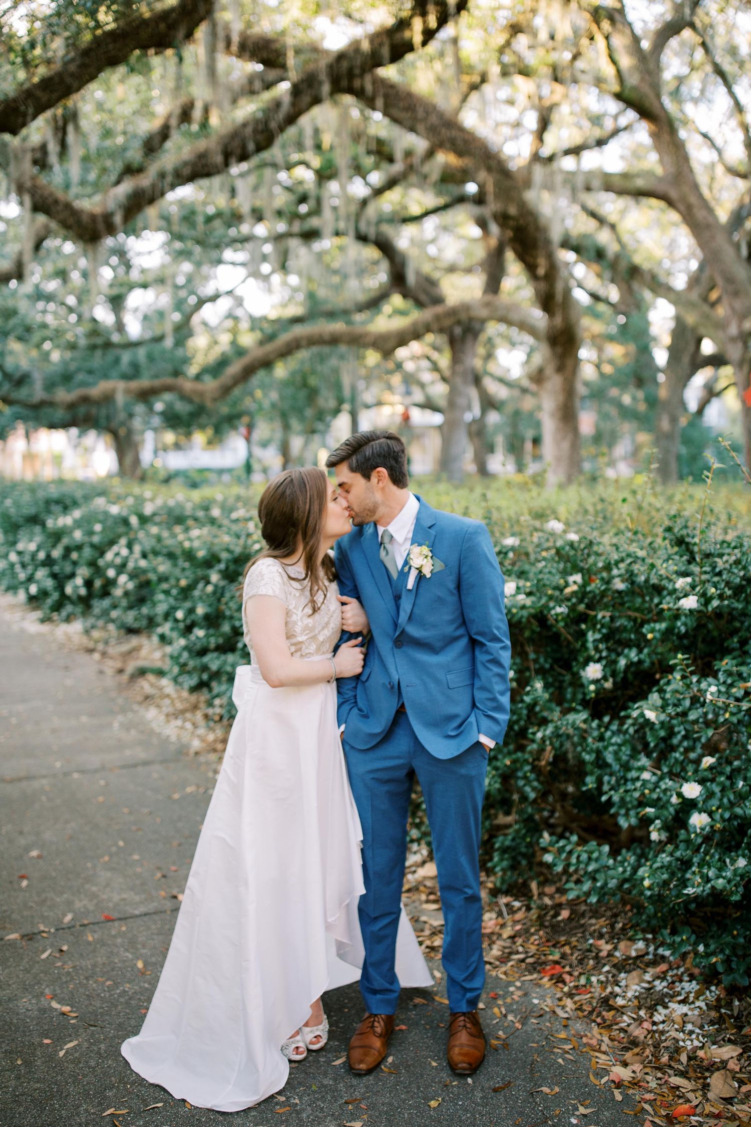 Intimate wedding portrait beneath Spanish moss-covered trees on garden path.