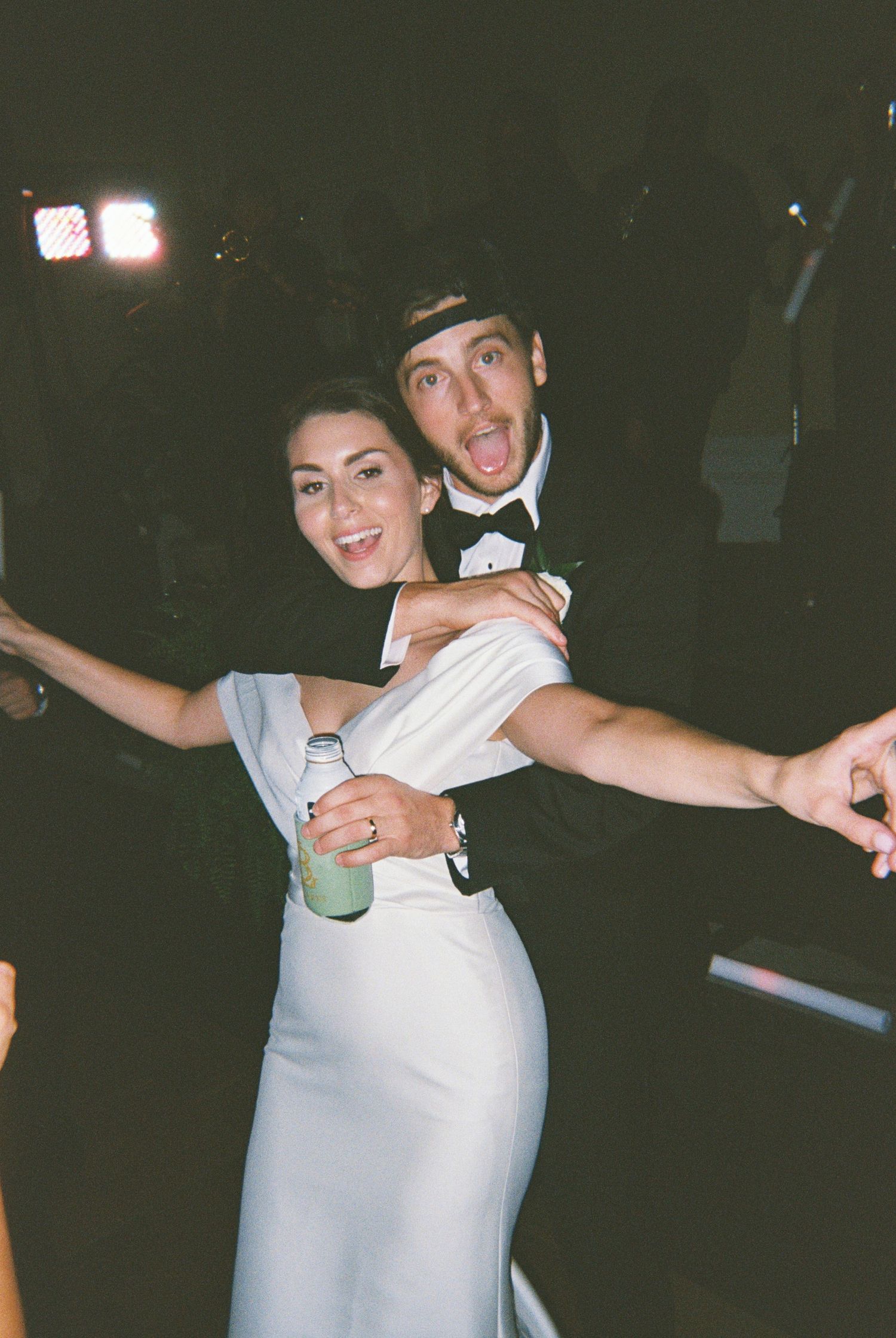 A couple in formal attire having fun at a party, with the woman in a white dress and her partner making an excited expression.