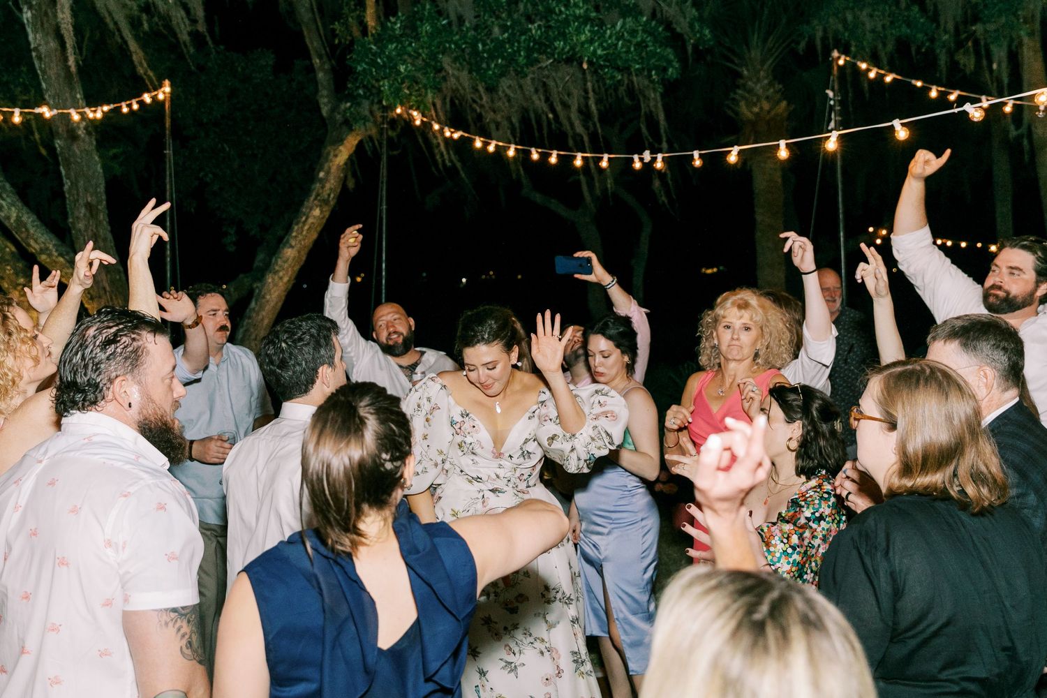 Wedding guests dancing outdoors under string lights at a nighttime reception.