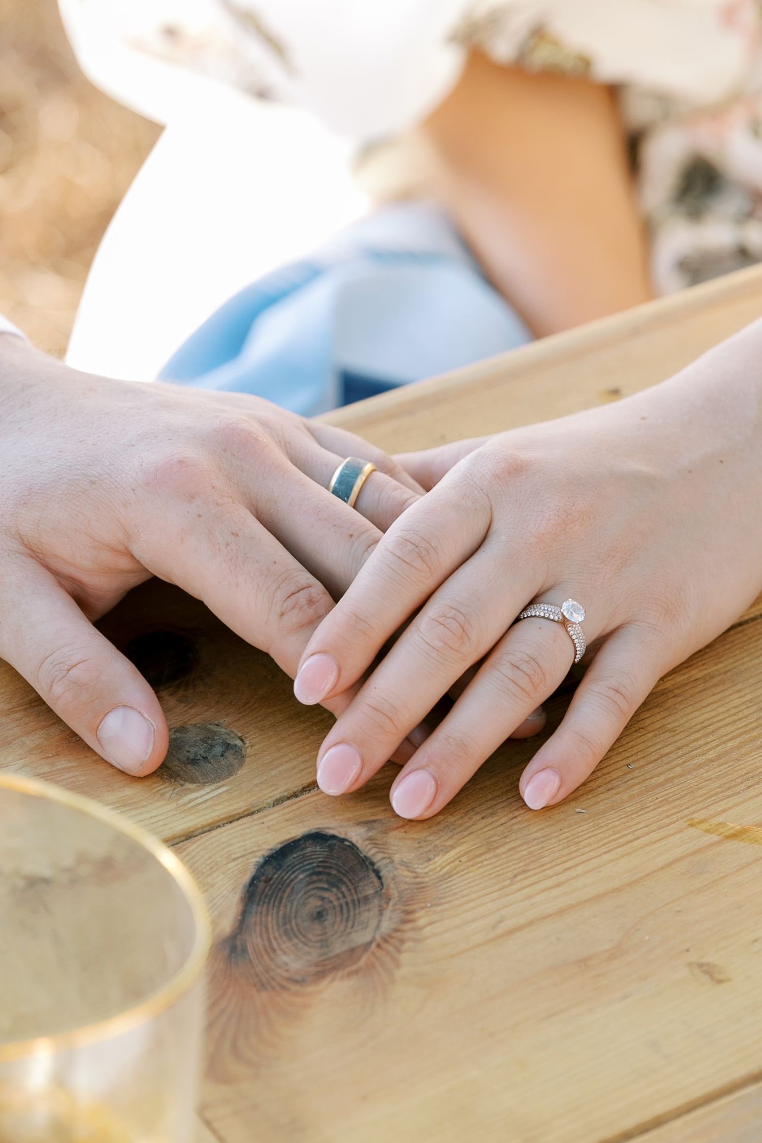 Close up of hands wearing wedding rings resting on a wooden table surface.