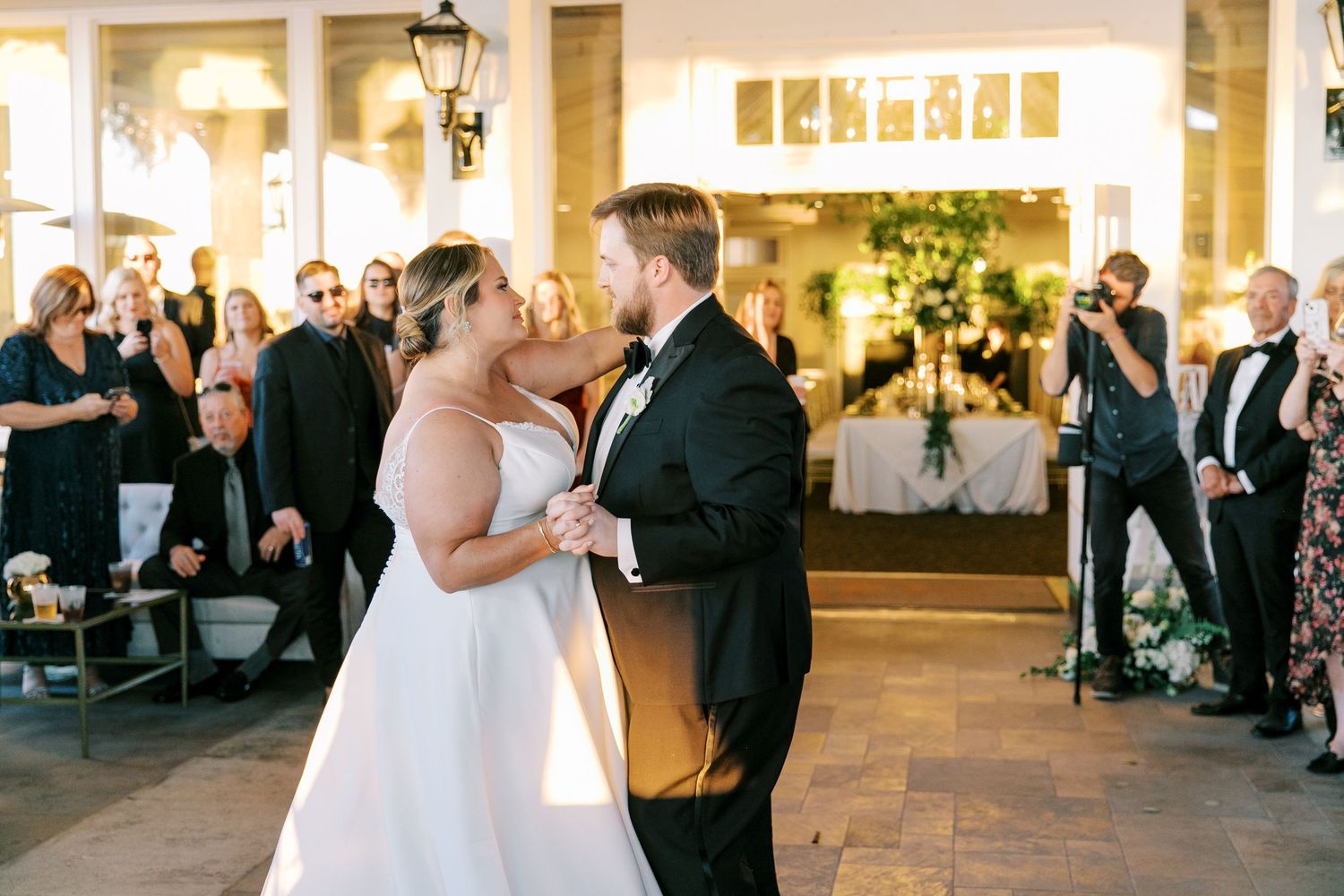 A romantic first dance at an elegant wedding reception with guests watching from the outdoor patio space.