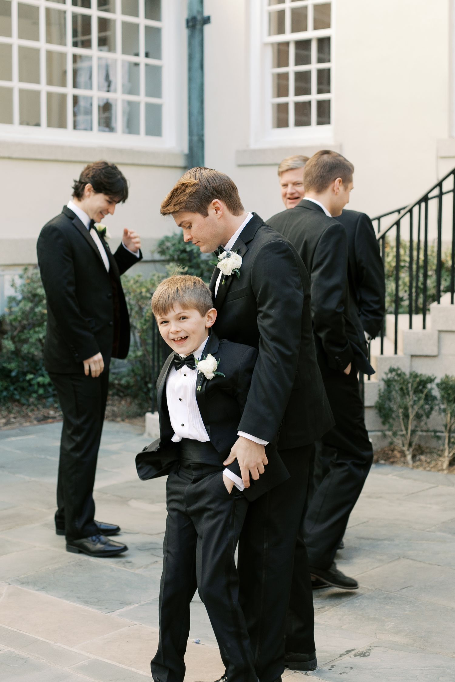 Young ring bearers in black tuxedos playing on church steps.