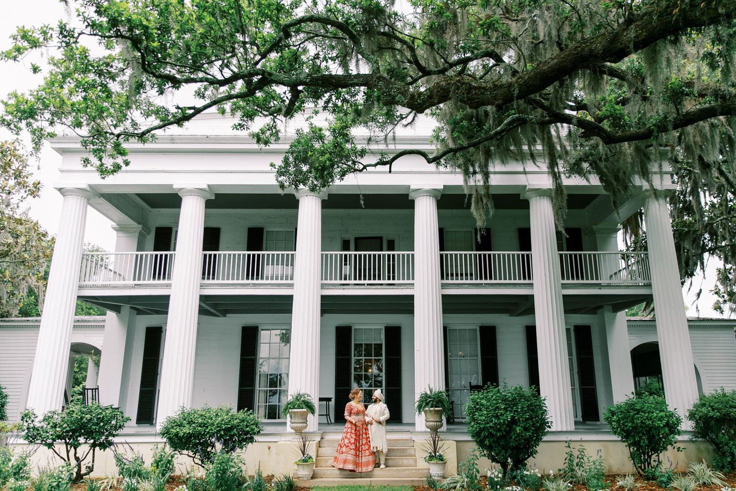A classic Southern mansion with white columns and wrap-around porches surrounded by oak trees at Beaulieu in Savannah, GA.