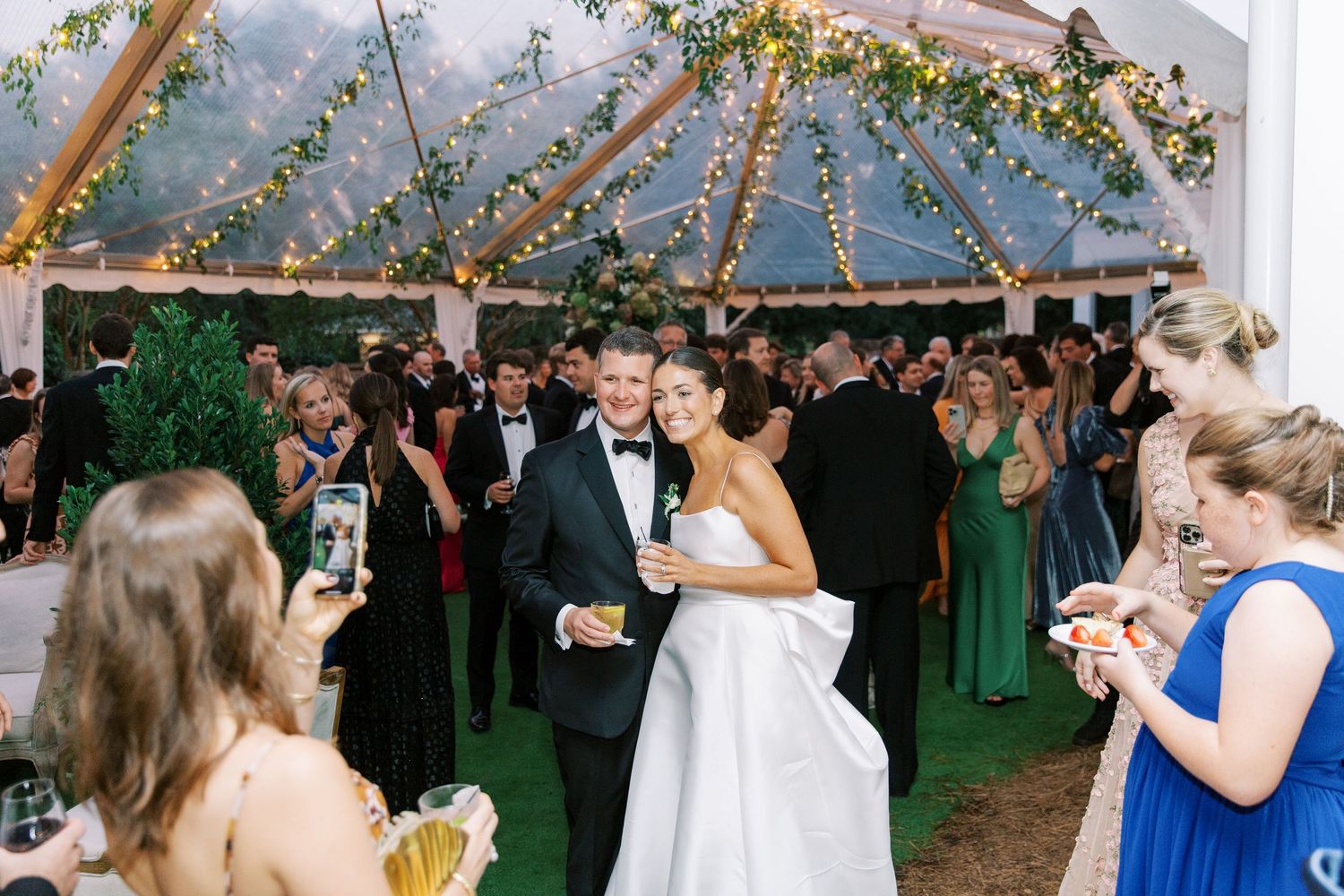 Romantic celebration under a tent decorated with twinkling lights and greenery at an outdoor wedding reception.
