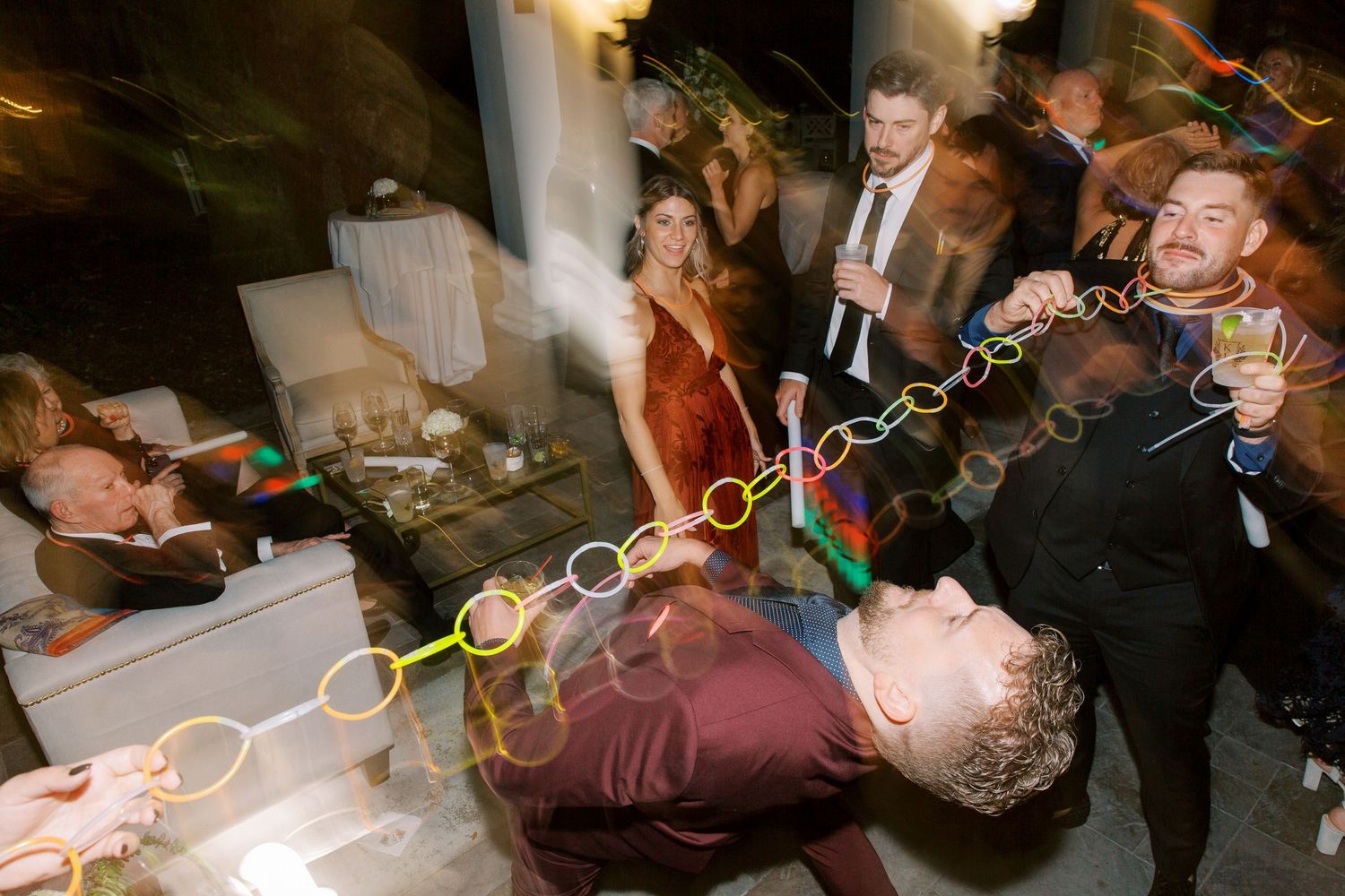 Party guests dancing and celebrating with glow sticks during a nighttime wedding reception.