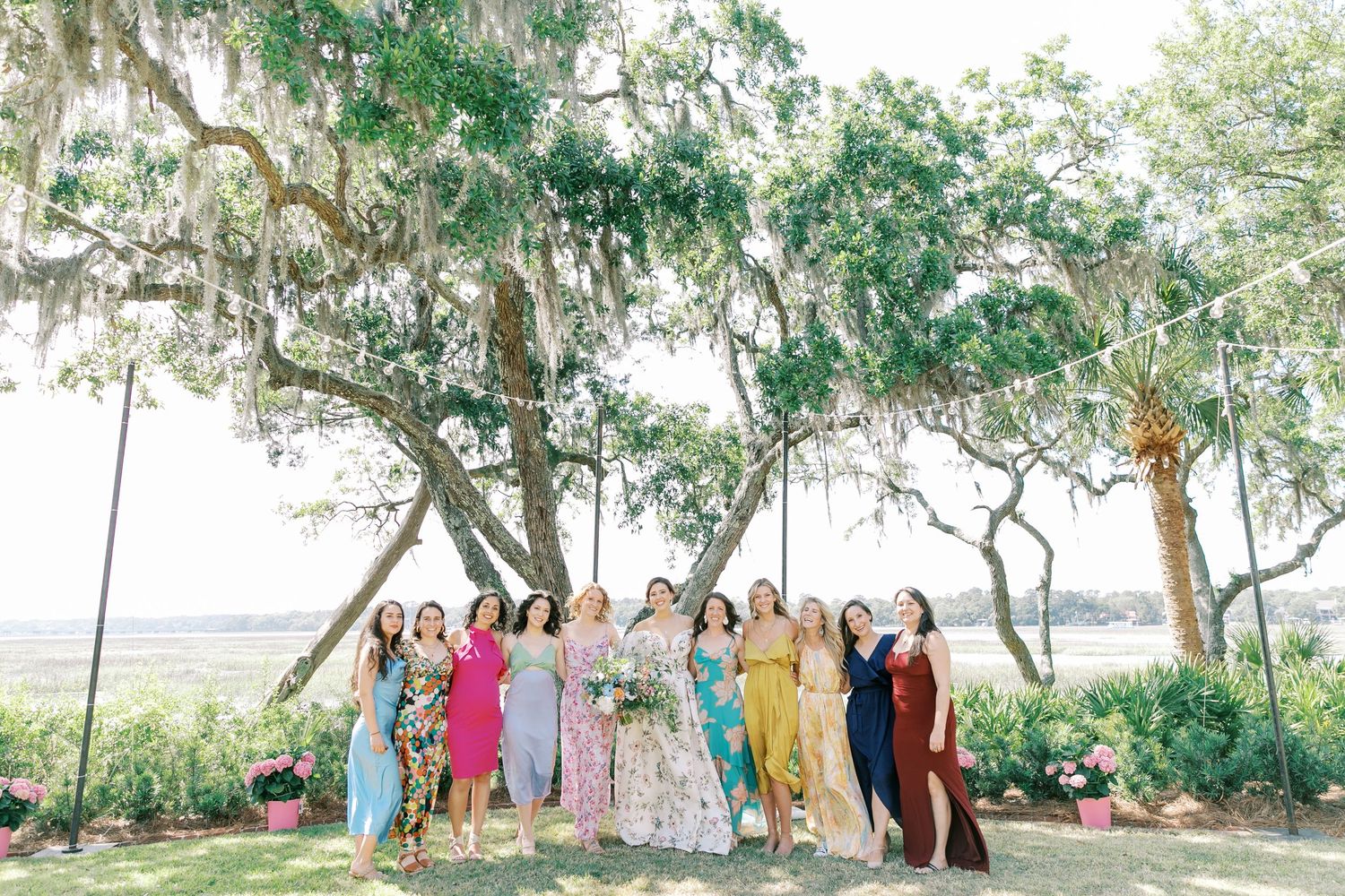 A panoramic view of colorfully dressed guests gathered under oak trees at an outdoor celebration.