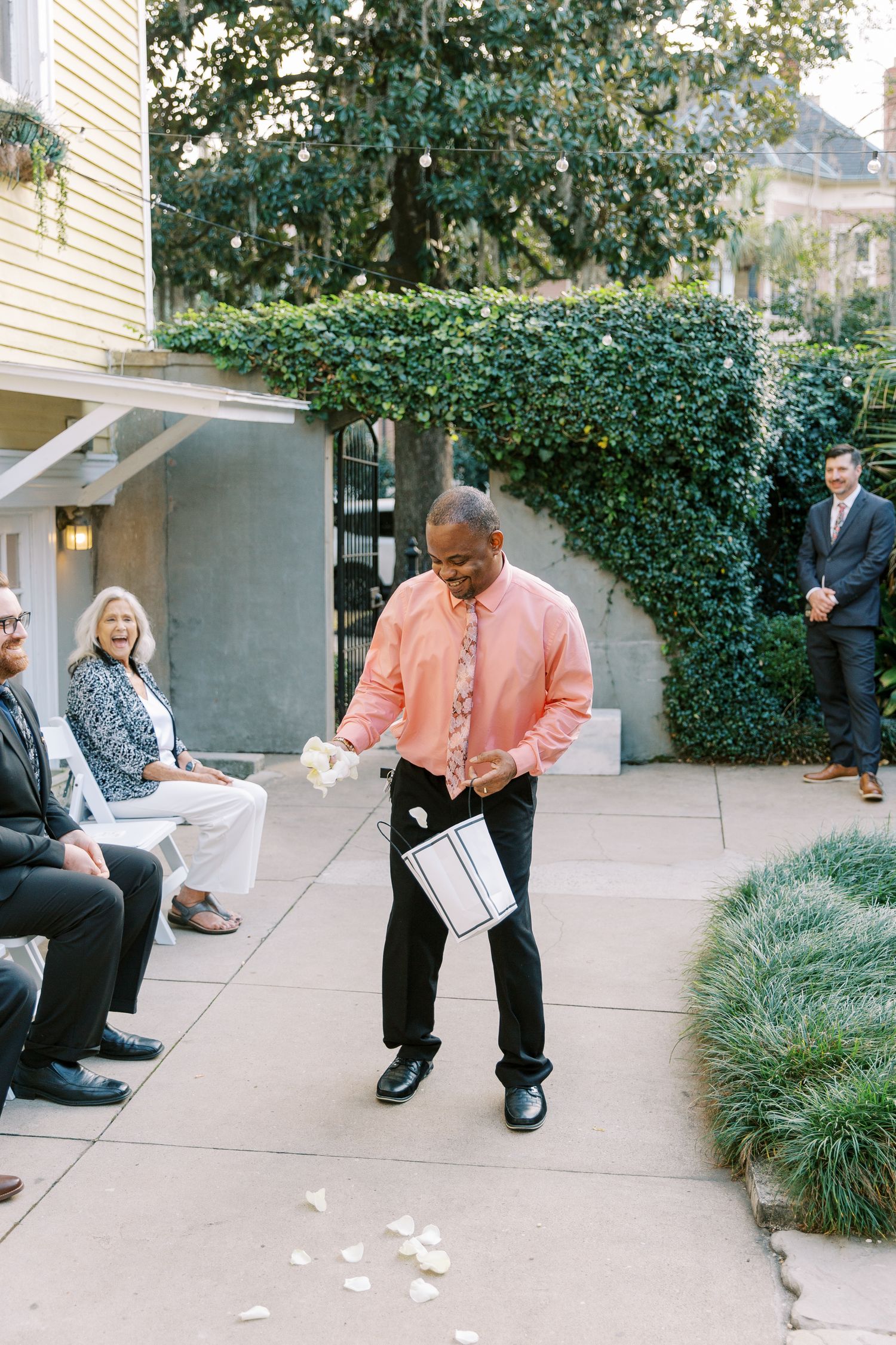 Wedding guests seated on outdoor patio watching flower petals being scattered.