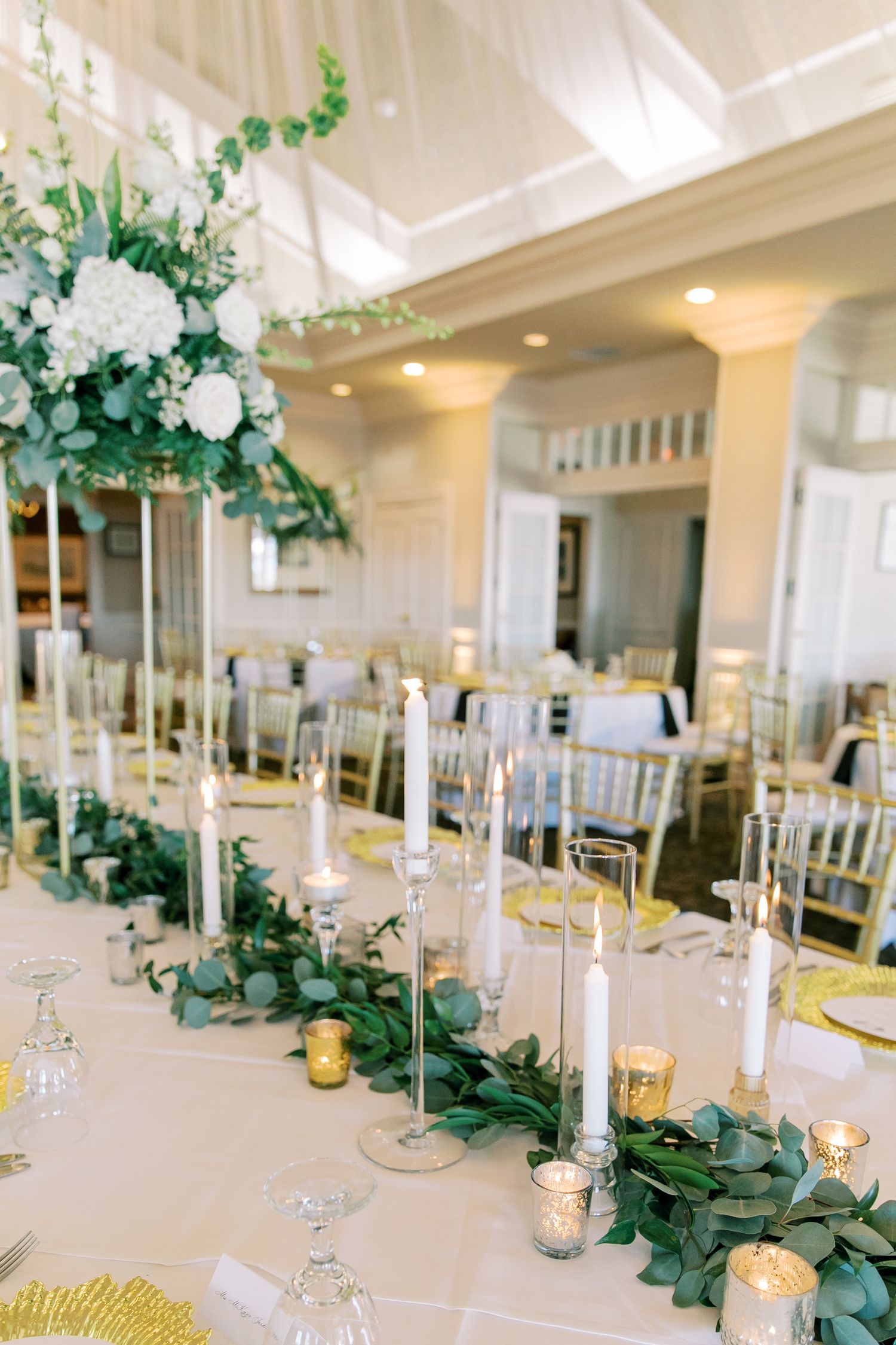 Elegant wedding reception table with white floral centerpieces, candles, and green garland runners.