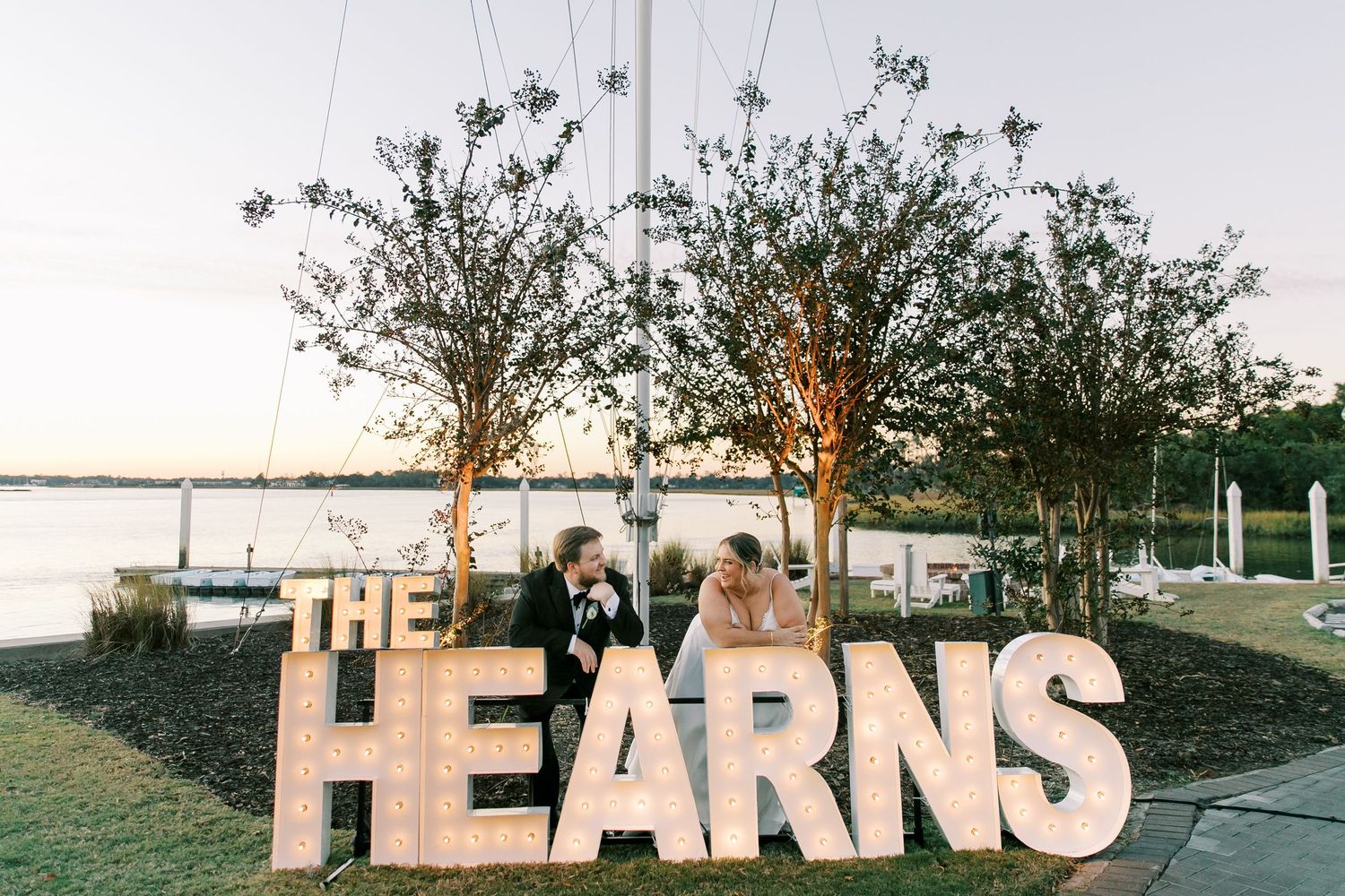 Large illuminated 'THE HEARNS' sign displayed at outdoor waterfront wedding venue at dusk.