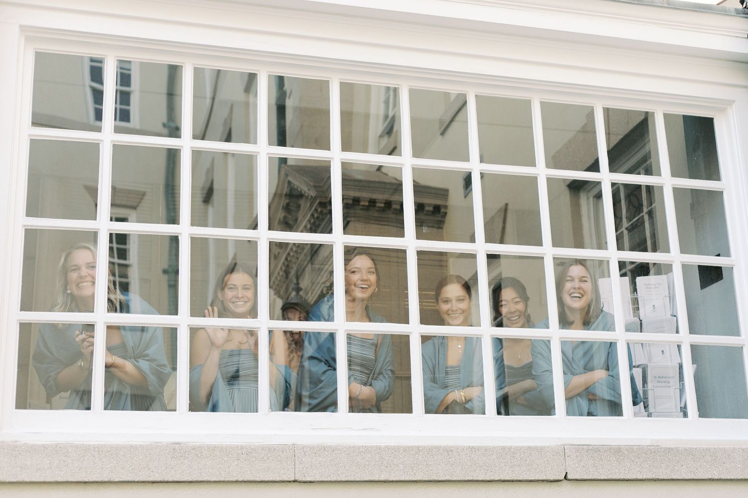 A row of windows in a white building with people looking out and smiling.